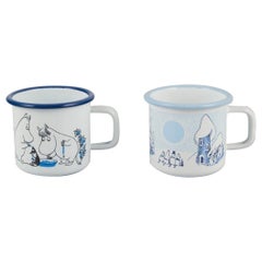 Muurla, Finland. Two enamel mugs featuring illustrations of Moomins