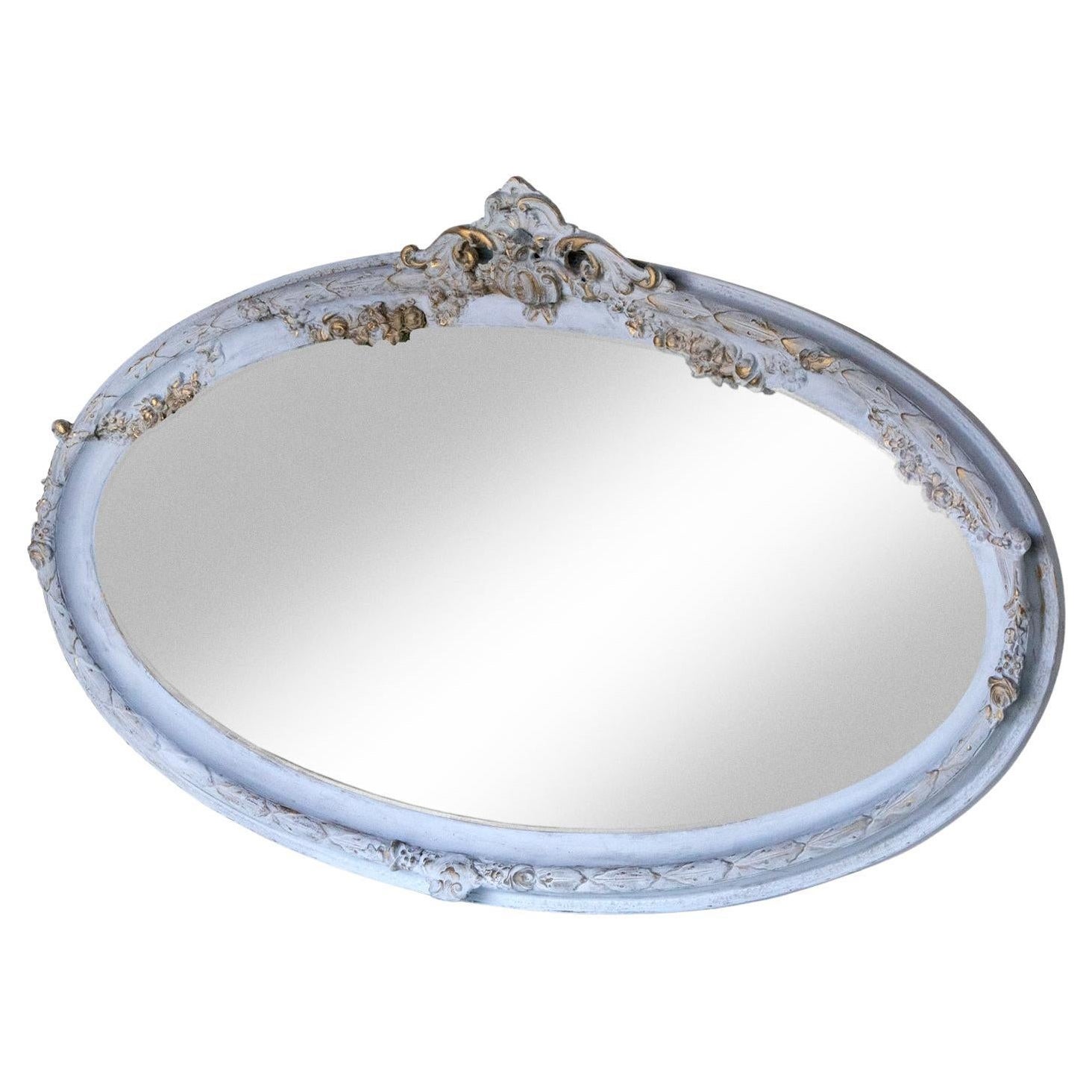 Cet adorable miroir ovale biseauté de style victorien est orné d'une crête détaillée, rehaussée d'or sur fond bleu français, et de détails décoratifs supplémentaires placés autour du cadre.    