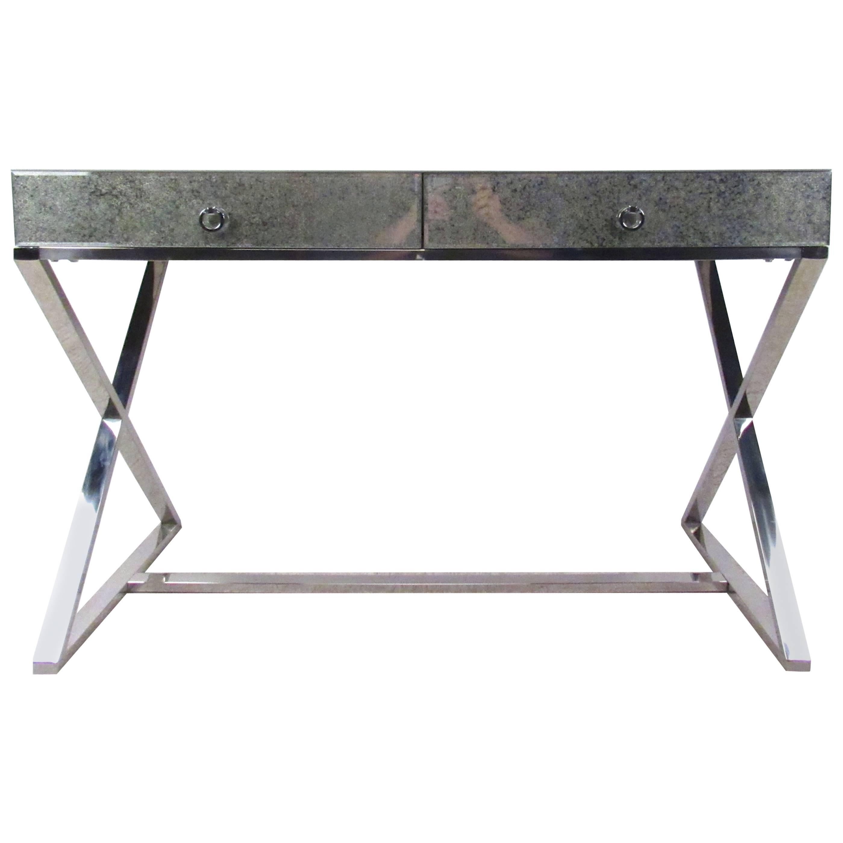 This unique antiqued glass writing table features a wonderful chrome X-style base and two drawer storage. Unique pulls, sturdy construction, and antique finish on the beveled mirror glass adds to the charm of the piece. Please confirm item location