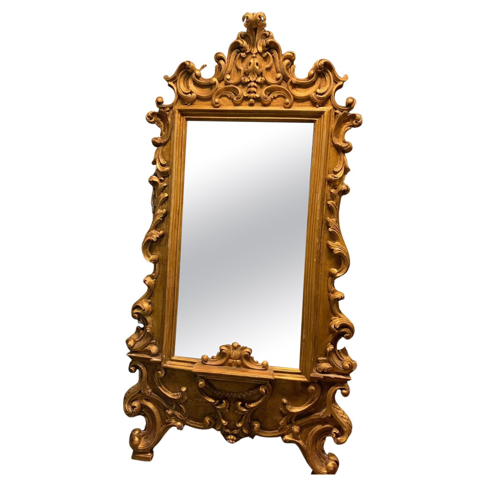 Floor mirror in gilded wood, richly carved with scroll decorations, Italy