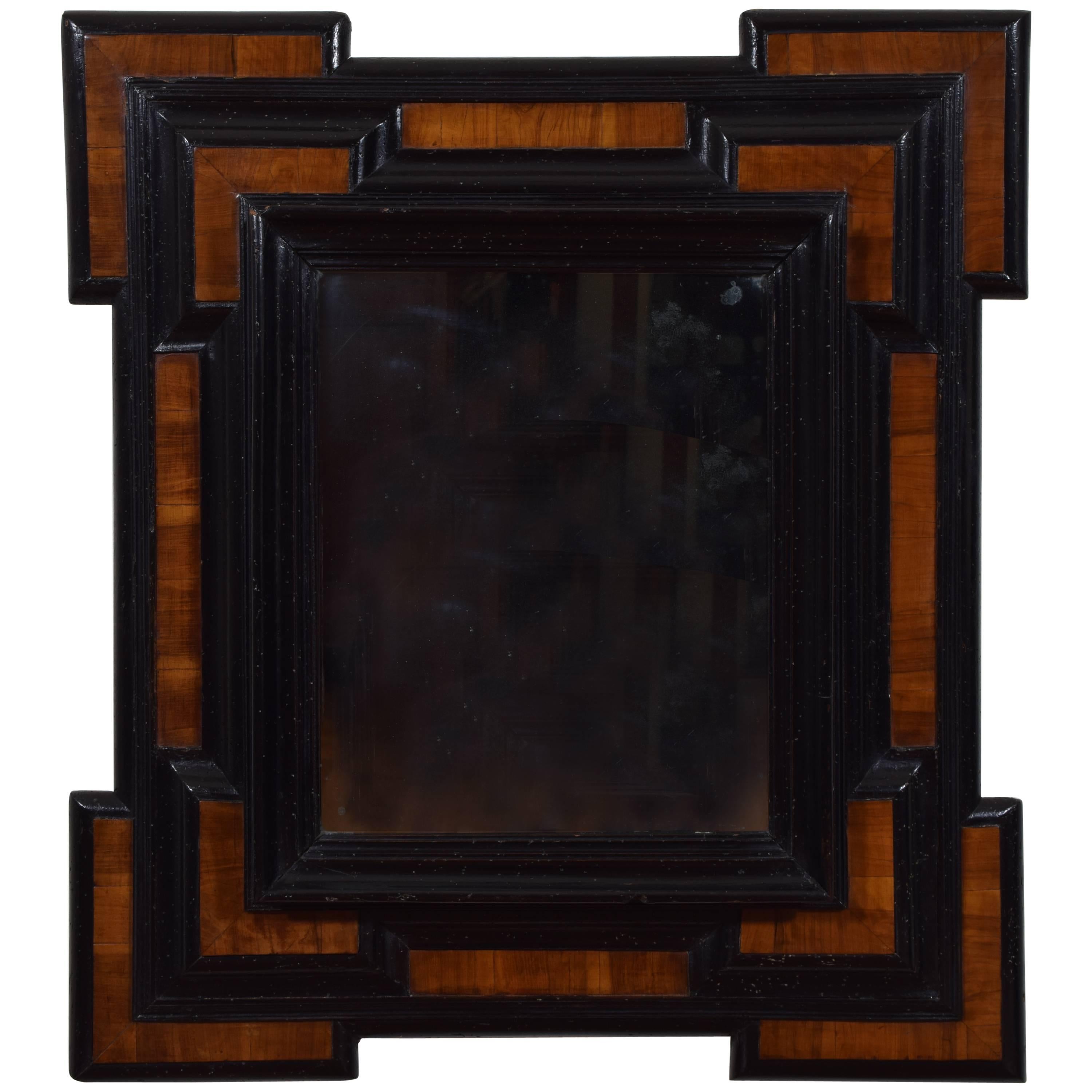 The stepped corners the lowest of sections that rise toward the middle in alternating sections of walnut veneer and ebonized surfaces, retaining antique mirrorplate.