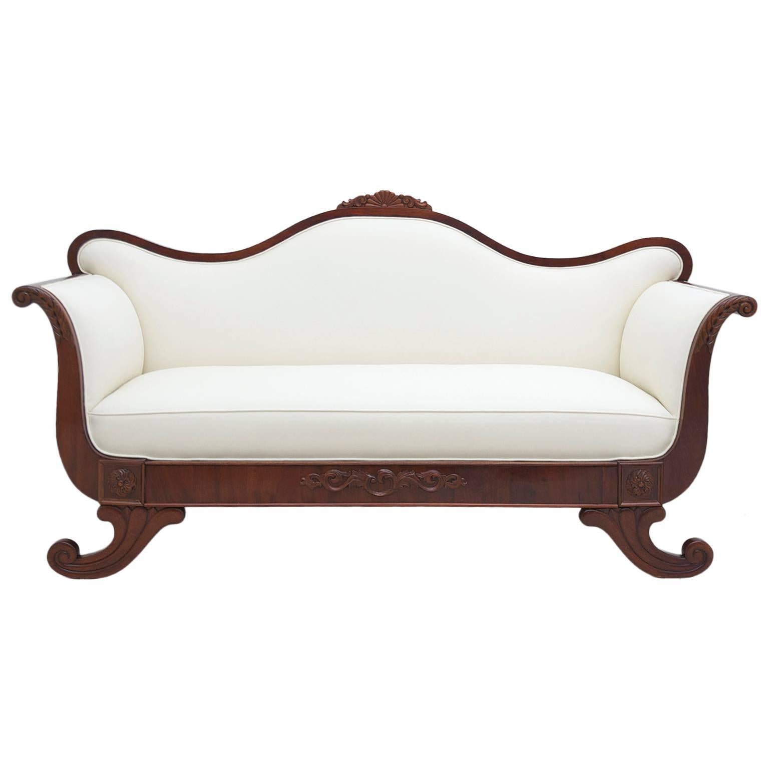 A beautiful and comfortable Swedish Karl Johan sofa or canape with scrolled arms, camel-back, and carved cornucopia feet, in French-polished West Indies mahogany, with cream-colored upholstered seat back and sides, Scandinavia, circa 1825. Jute