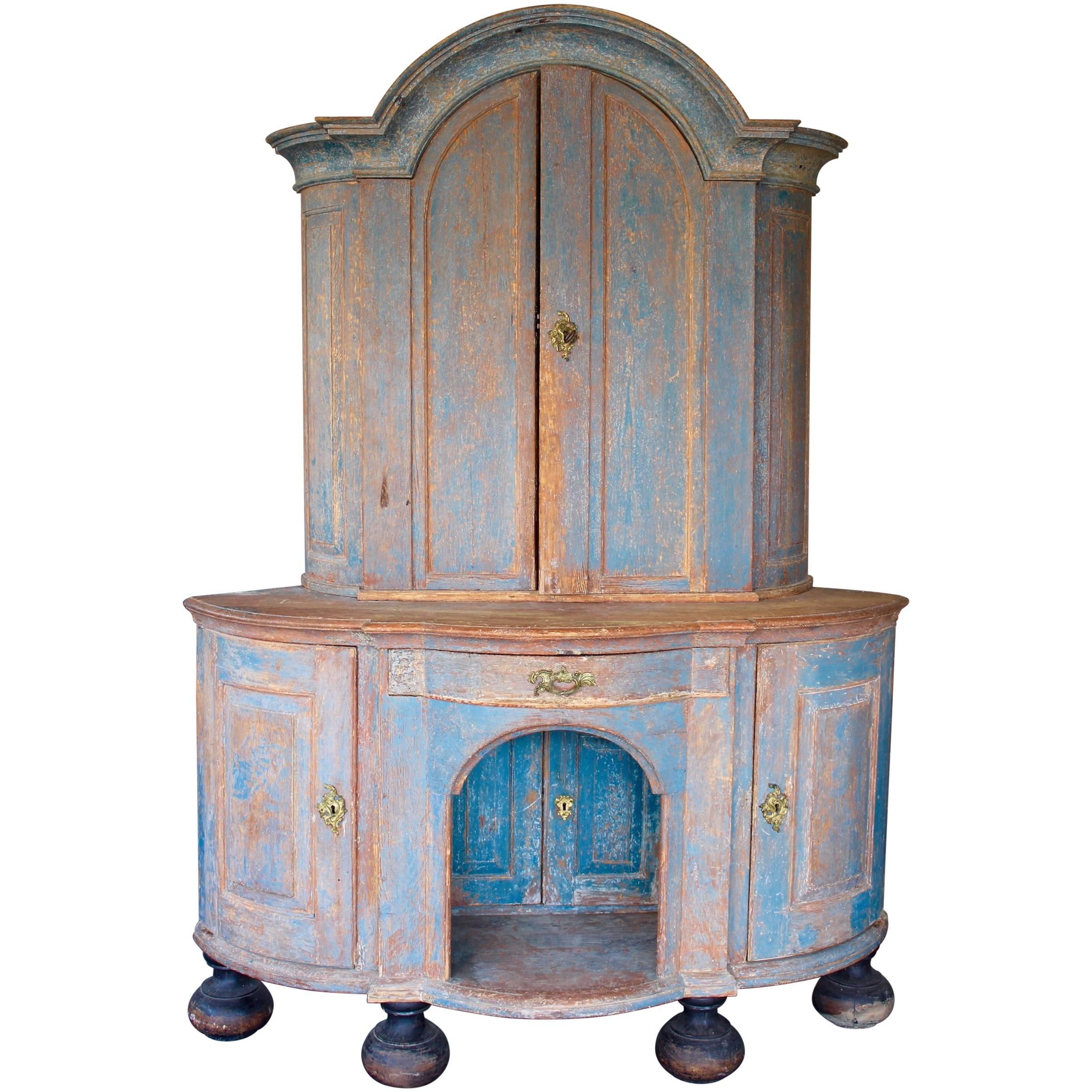 Curved form with shaped and molded cornice, four doors with internal shelves, one drawer and a recessed shelf, blue paint.