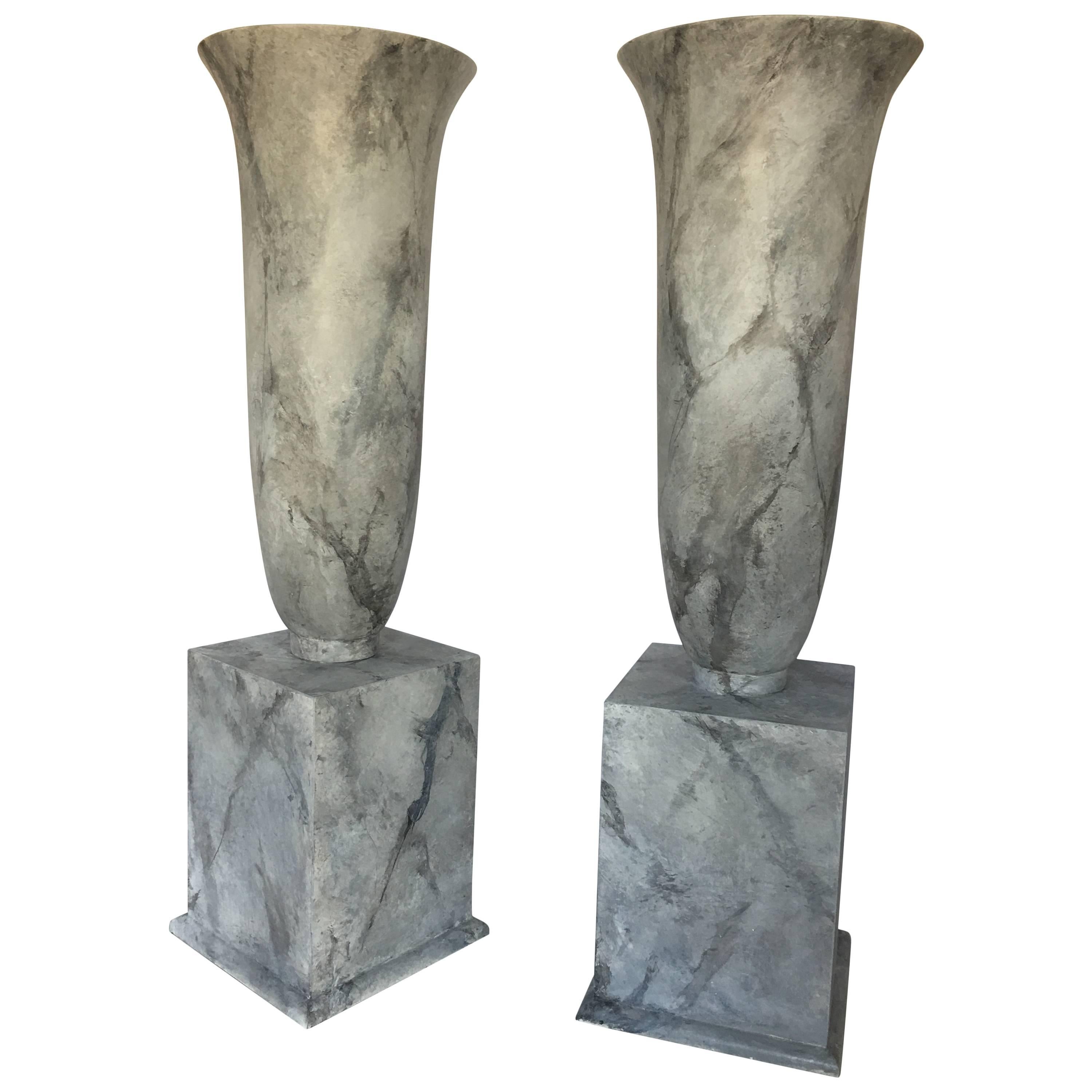 Dramatic lightweight resin urn shaped vessels featuring a realistic hand-painted honed Carrara marble faux finish. Classically inspired modern shaped vases sit on top of detachable plinth bases. These statement pieces are gorgeous displayed on the