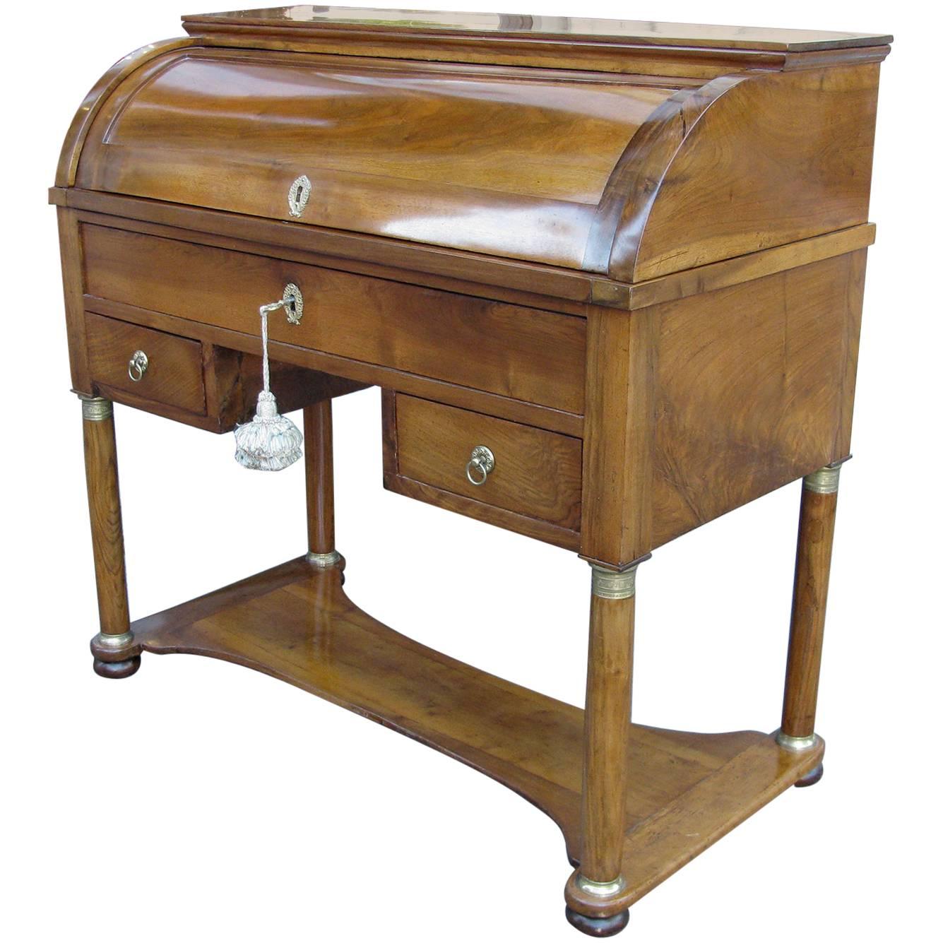 An early 19th century Empire walnut bureau of Italian origin. A cylinder front, opening to reveal an arrangement of small drawers and compartments, below a pull-out writing leaf, a large useful drawer and a knee hole flanked by drawers decorated