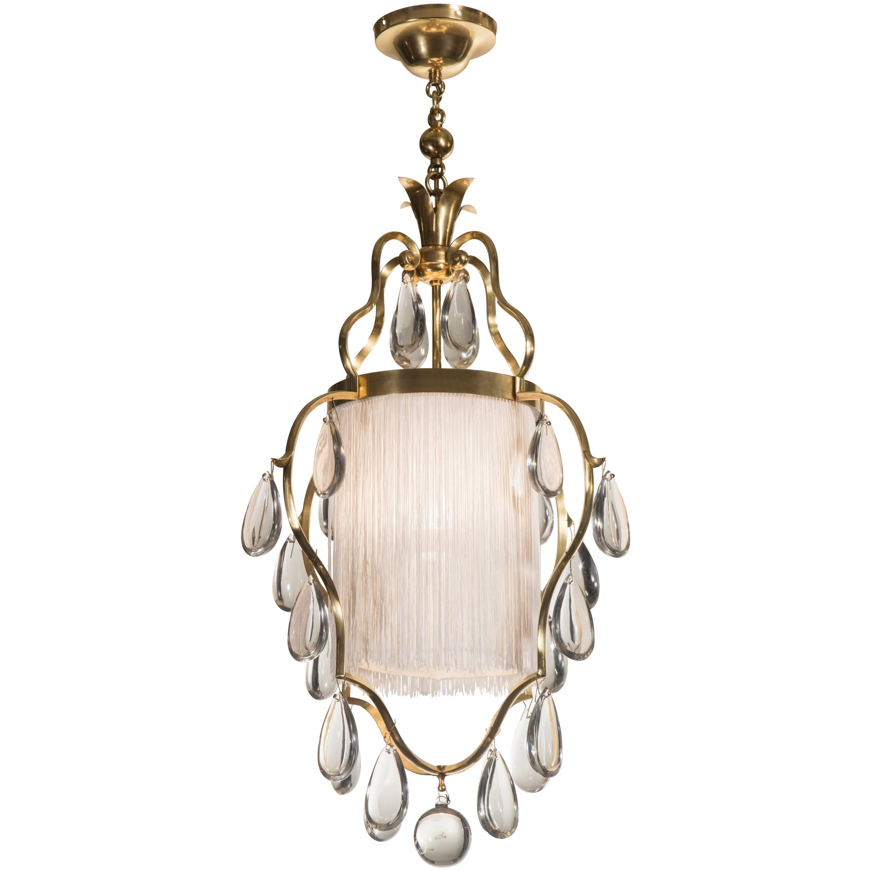 A graceful and exuberant chandelier of the highest quality. The shaped body consisting of four scrolls hung with clear faceted pear-shaped crystals, enclosing a silk shade hung with tassels, terminating in a glass sphere. 

A related chandelier is