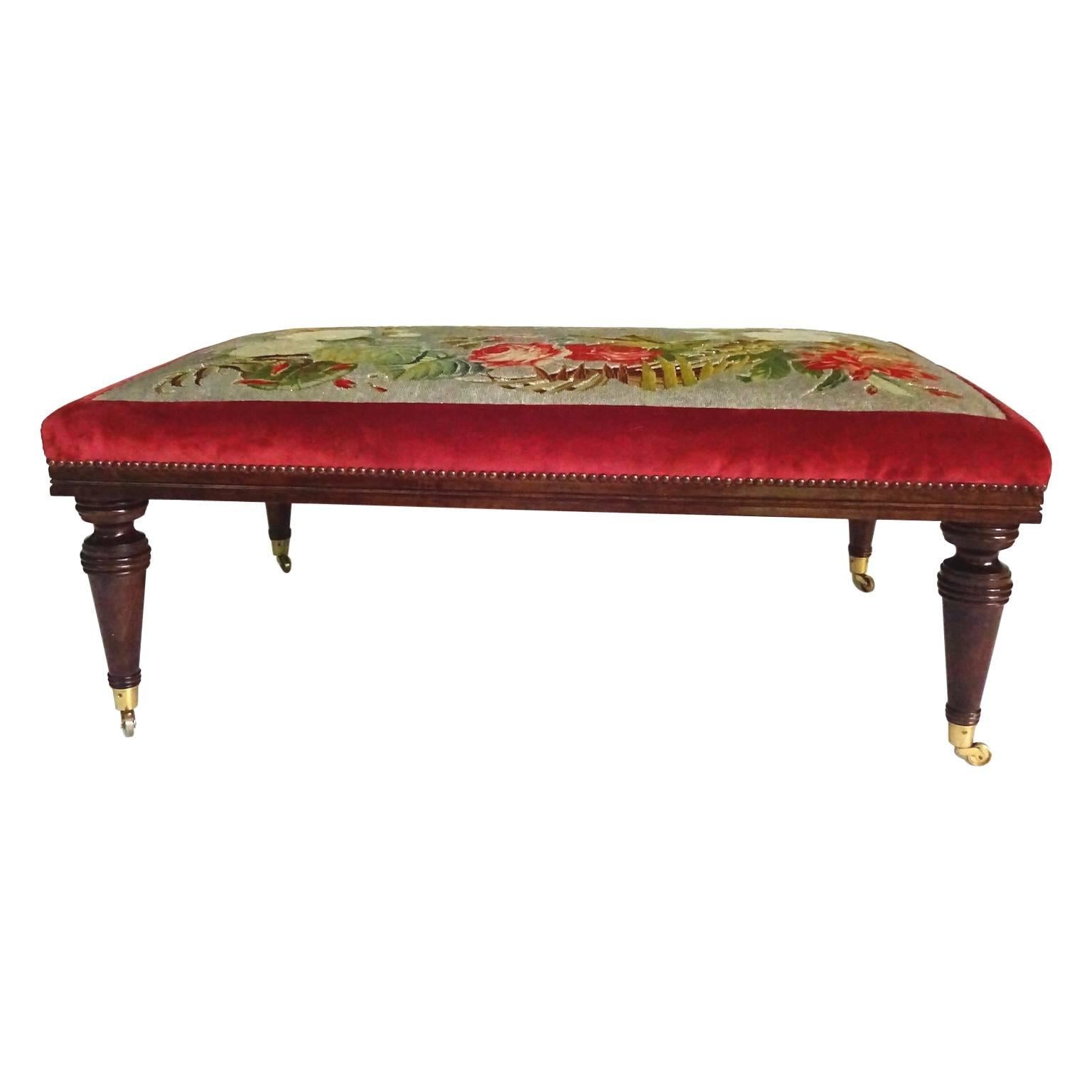 Large Victorian mahogany bench or stool with intricate floral beaded needlework. Needlepoint framed in wine red velvet and anchored with large brass upholstery tacks. Nice turned leg raised brass casters.