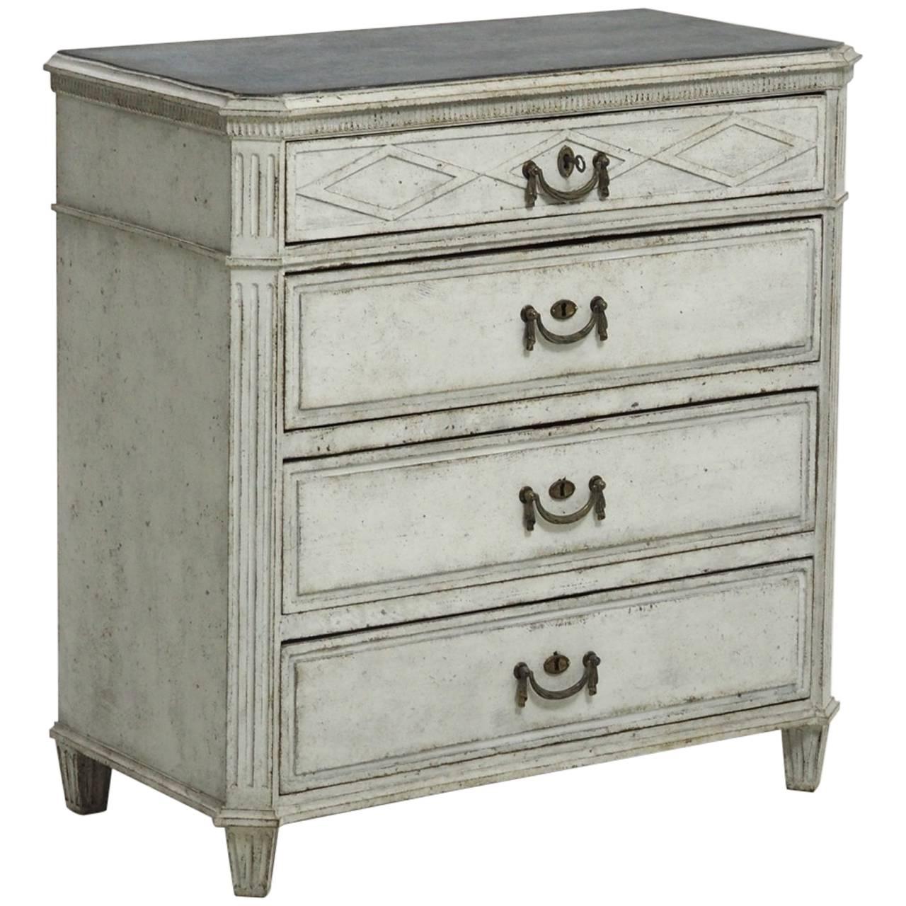 A classically carved Swedish Gustavian painted chest featuring a carved lozenge design on the top drawer, fluted corner posts, tapered and fluted legs, and brass swag motif drawer pulls.

The Gustavian style, named after King Gustav III of Sweden,