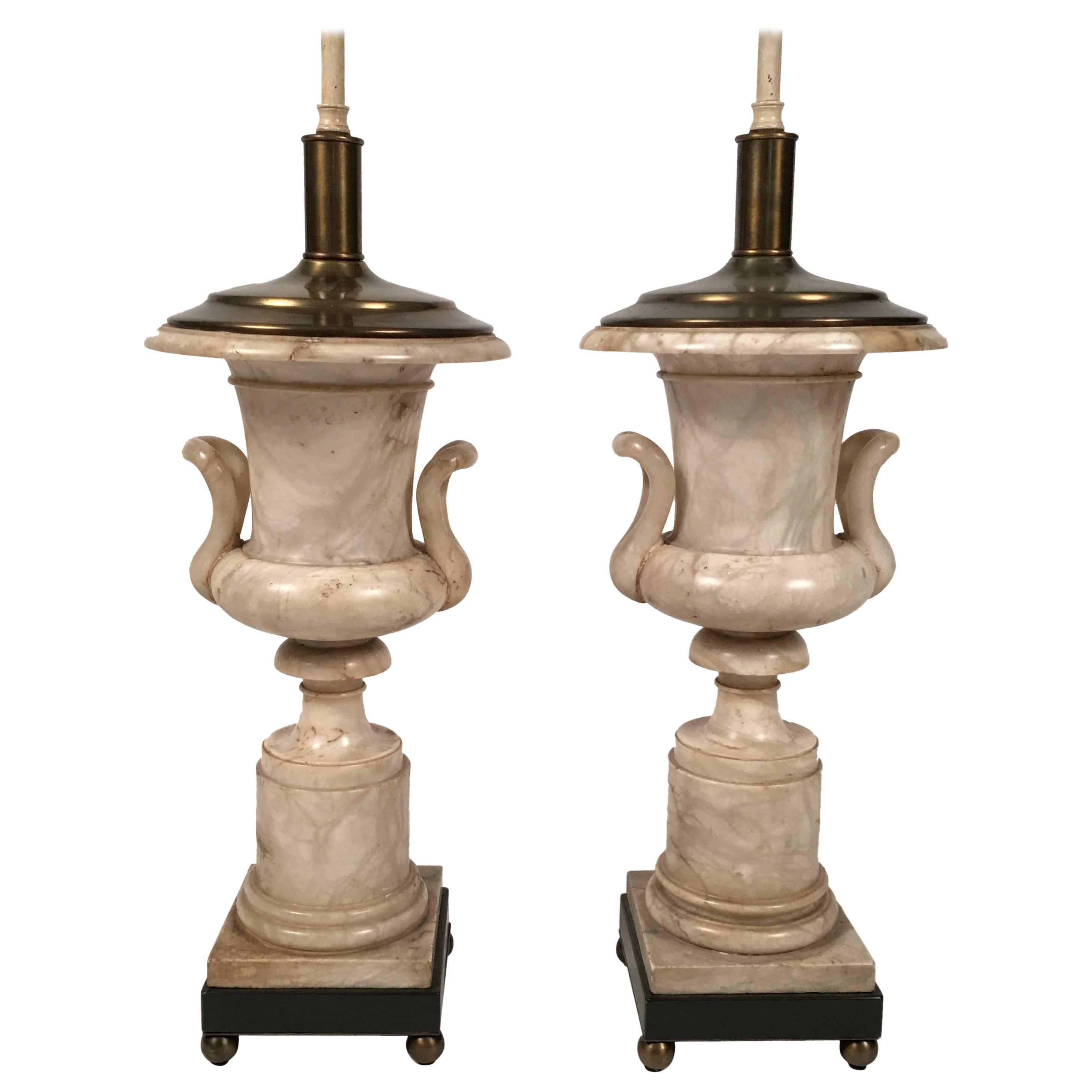 A pair of Italian Neoclassical style marble campana (bell shaped) urn-form lamps in alabaster, each mounted on charcoal grey wood bases with brass plates underneath, raised on four brass ball feet. Ceramic ball finials. New linen shades with bands