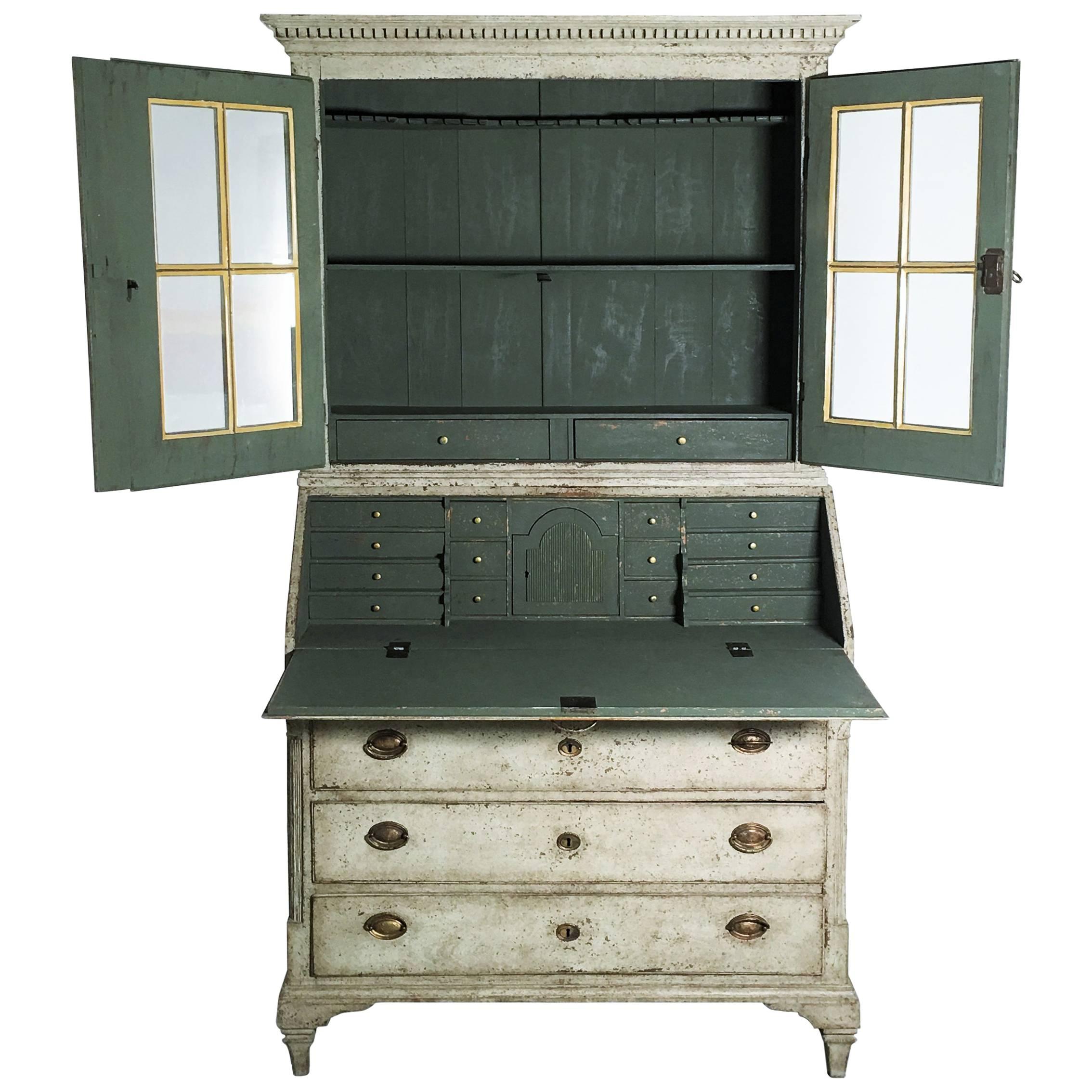 This is a rare and important Swedish Gustavian style painted secretary buffet with original brass hardware and locks, circa 1850. The upper china cabinet section has three shelves, the top shaped and slotted for spoons, behind door fronts carved