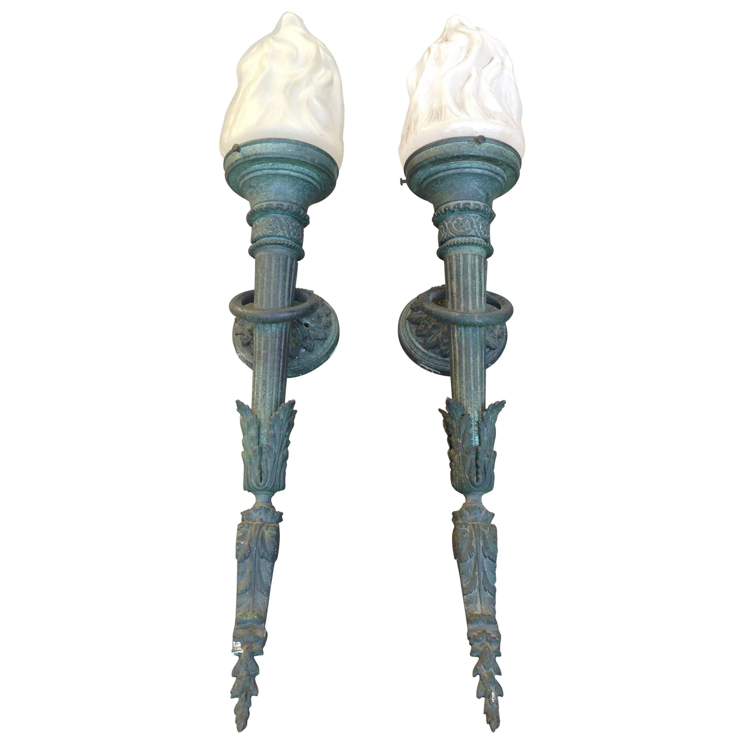 A pair of Beaux Art torch sconces in verdigris finish. Opaque glass flame form shades (slight variations to glass). Requires electrification.