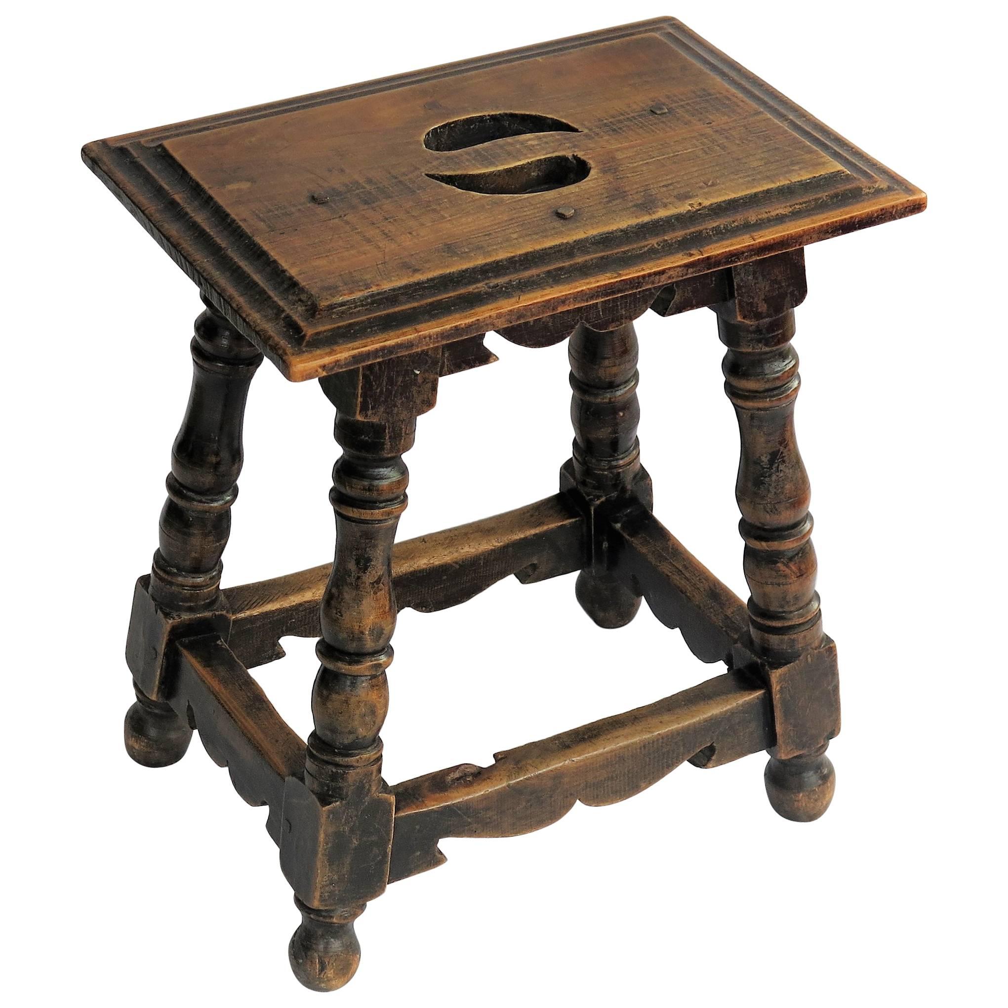This is a very good, well-made country stool from the early part of the 19th century which we attribute to a French country maker.

The stool has a chamfered rectangular top which is pegged to the base and has two hand cut-outs to the top. It has