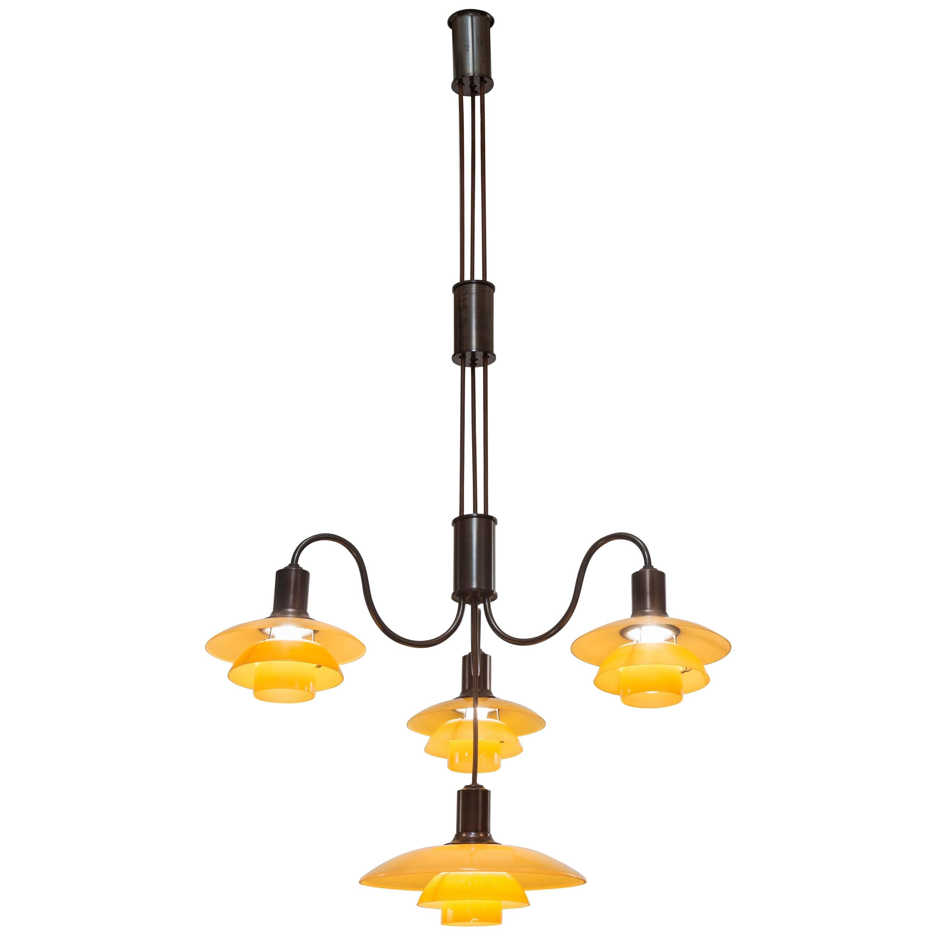 Adjustable height chandelier in very good condition. The cylindrical canopy, suspending two height-adjusting cylinders of patinated brass connected by cords, the bottom cylinder issuing three graceful s-curved arms, each arm with a 2/2 yellow