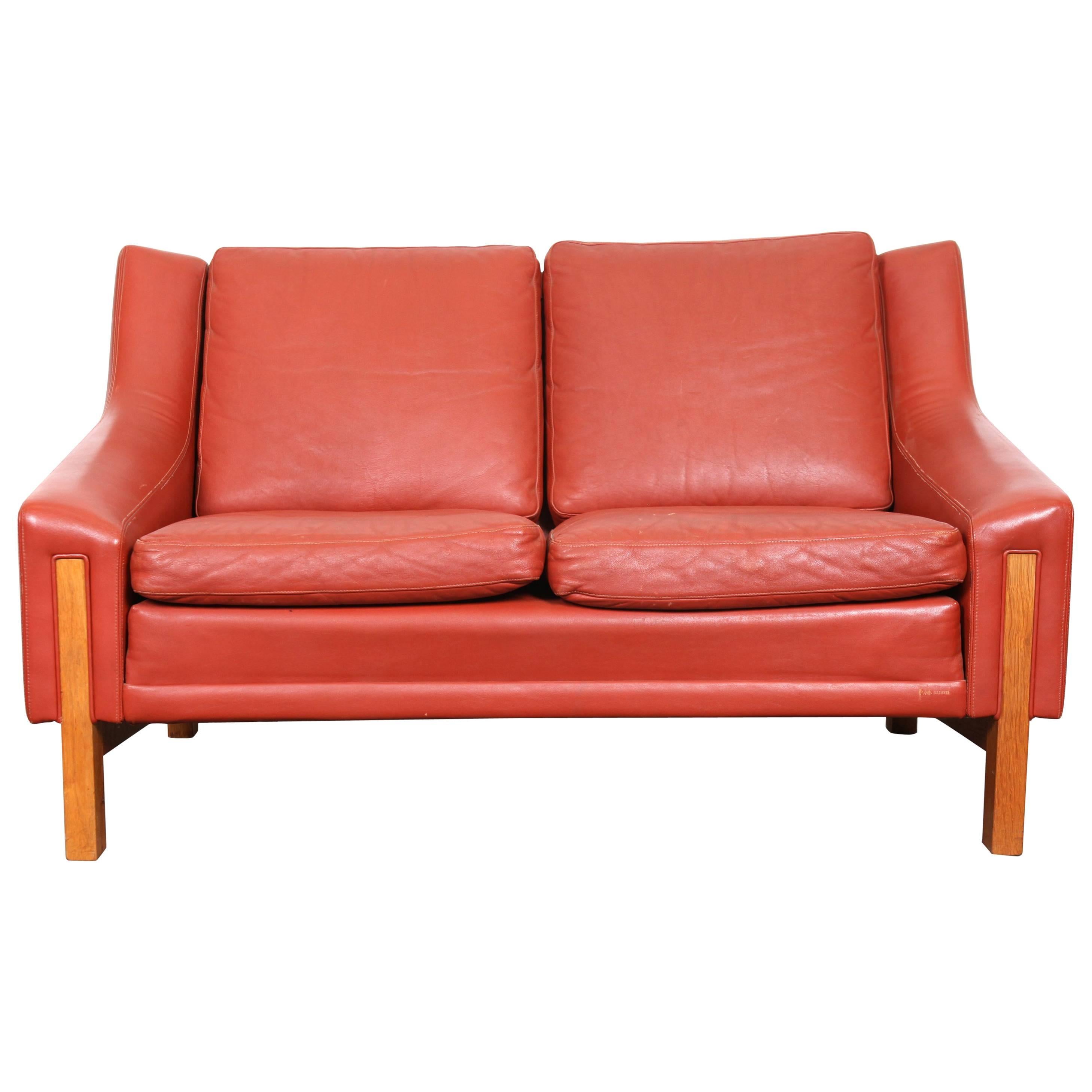 Red leather Mid-Century Modern love seat with wood accent legs.