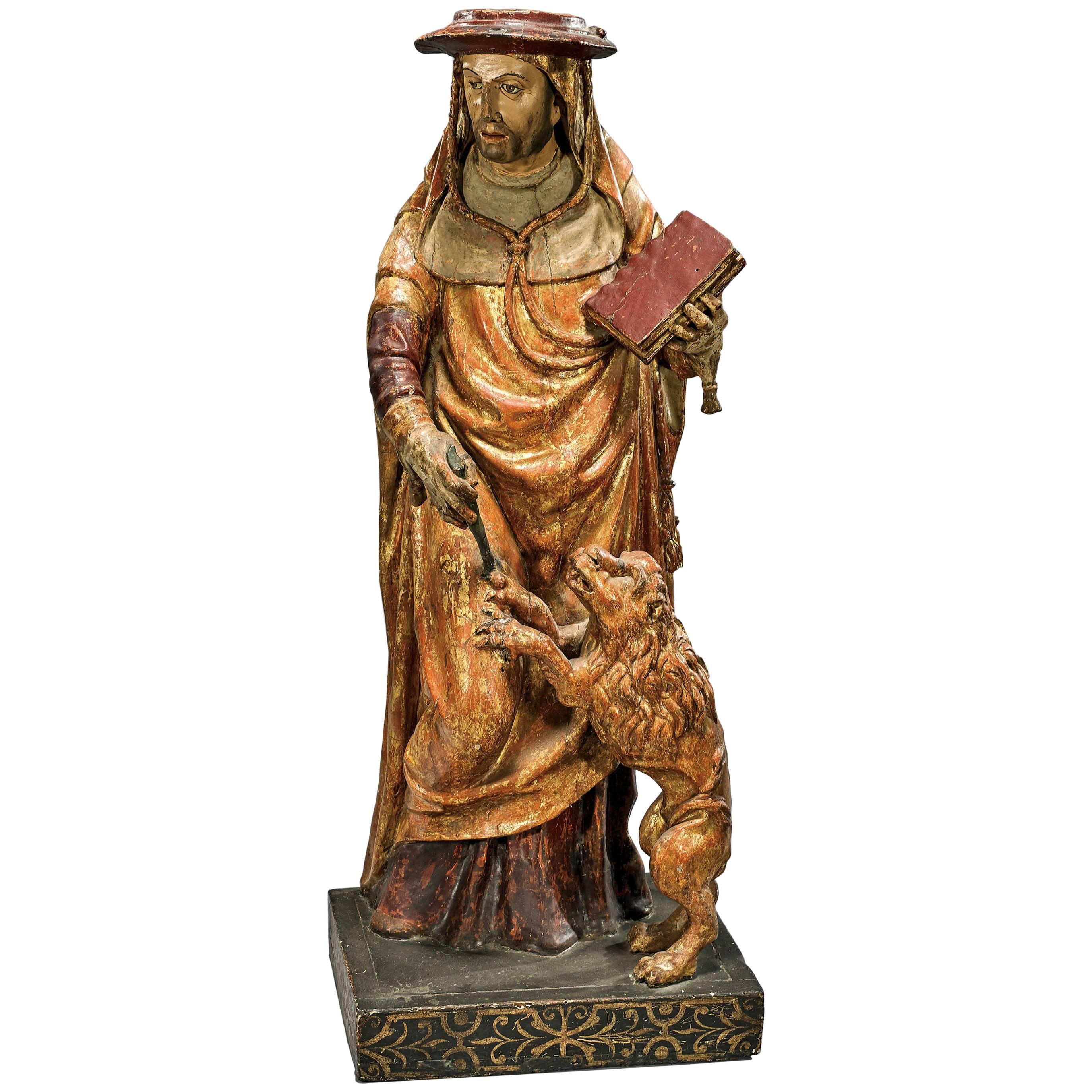 Antique Spanish colonial, carved and gilt gessoed wood figure; depicting a saint in gilt orange robes and a flat-topped hat; holding a book with a lion at his knee; on integrated base, 18th-19th century.