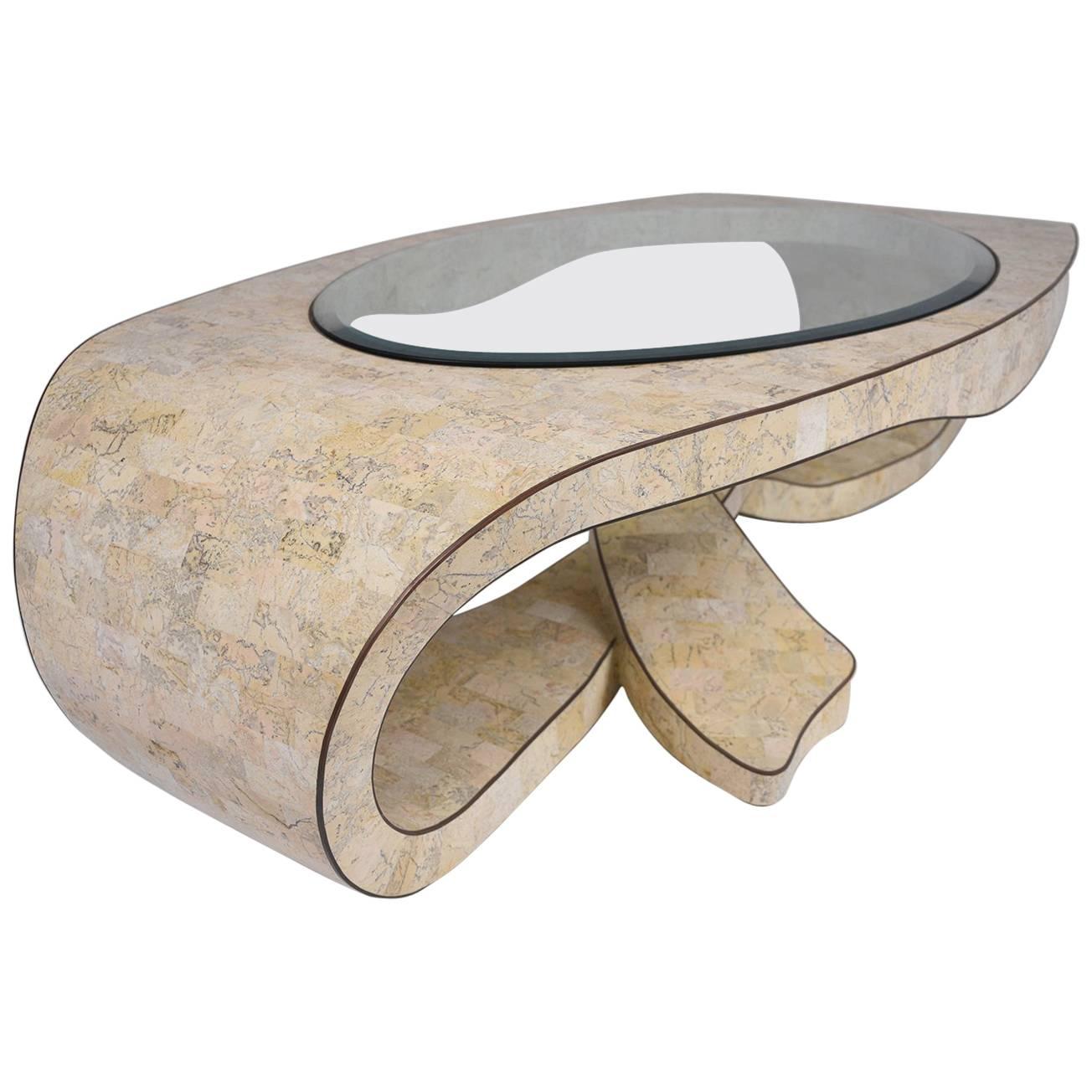 This unique 1970s vintage coffee table is made by Maitland-Smith Tessellated. The coffee table features a frame made from stone and glass with brass moudling details around the edges. The unique shape of the frame overlaps at the center of the base