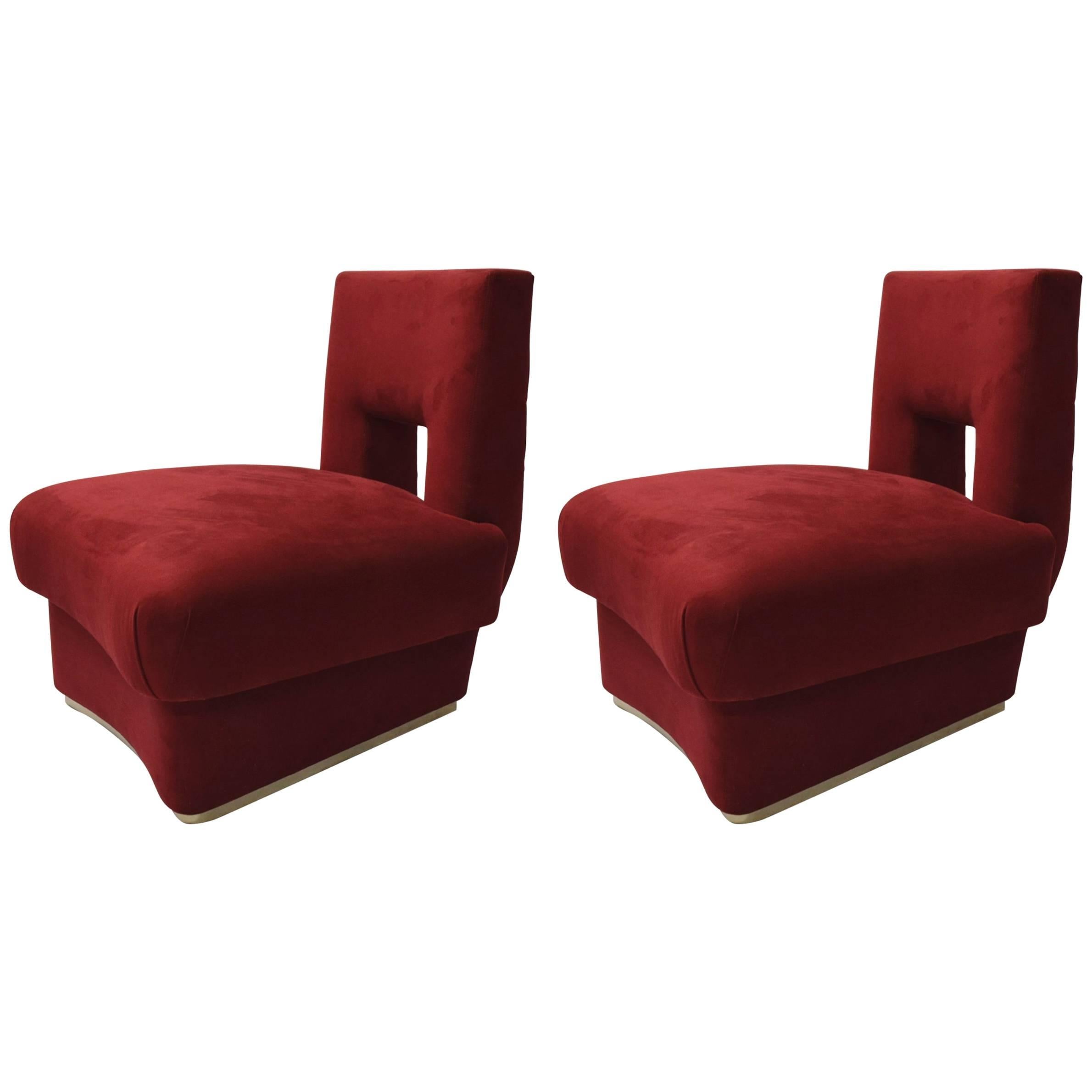 Pair of armless, Deco style lounge chairs upholstered in burgundy microsuede with a cutout detailed back rest and a curved seat and platform base that has a polished metal bottom border.