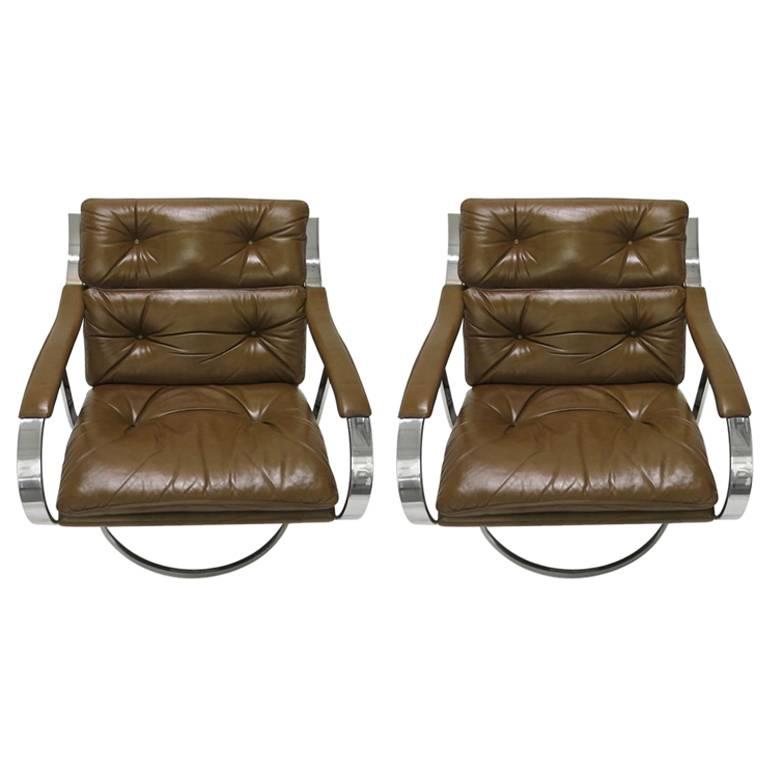 Armchairs designed by Gardner Leaver comprise solid polished steel frames, original brown tufted leather seats and upholstered arm rests, pleated leather detail on the back, curved arms, and a round base with a center stretcher that connects to the