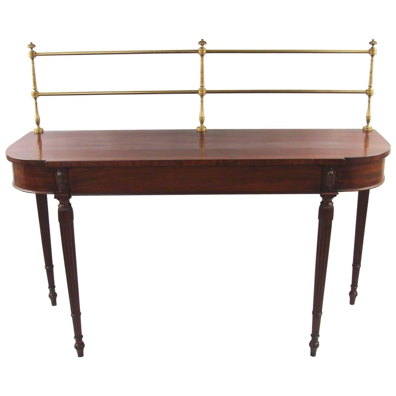 A compact George III period Sheraton design bowfront mahogany server retaining its original brass gallery, the shaped top with curved sides supported on fluted legs headed by well-carved paterae. Circa 1800.