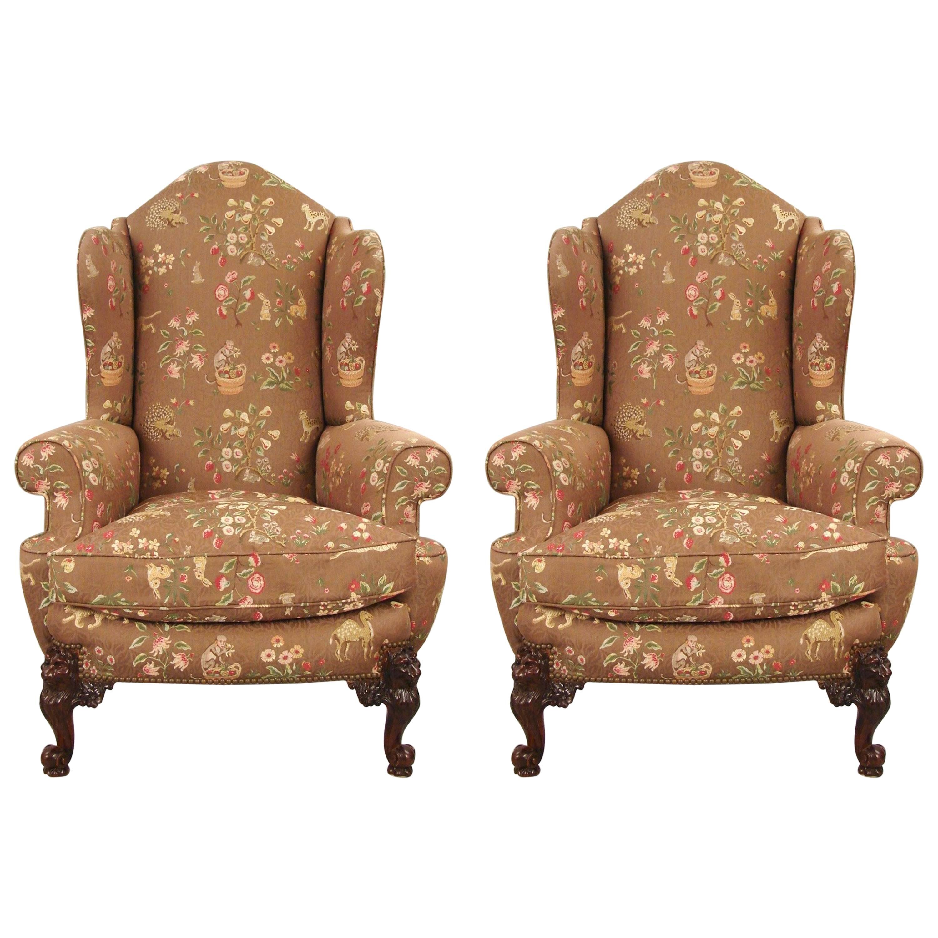 A fine pair of English mahogany wingback armchairs upholstered in an Anglo-Indian style silk or satin fabric with overall small exotic animal upholstery, the well-carved short cabriole legs carved with lion's faces flanked by floral rosettes.