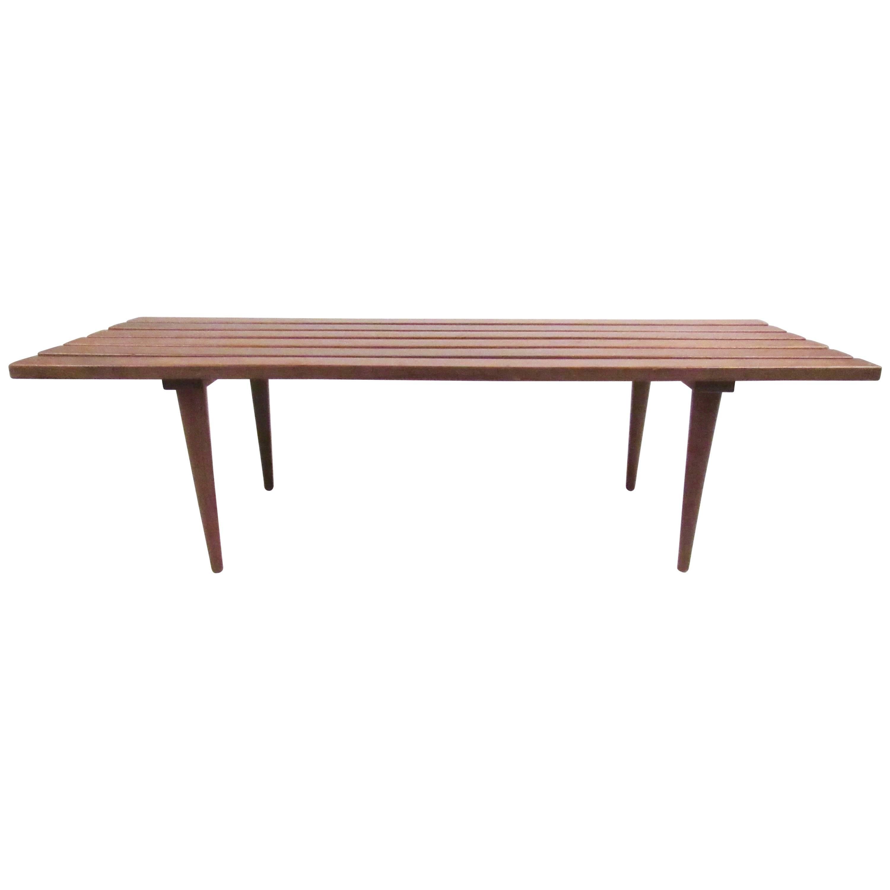 Cette table basse à lattes vintage présente une construction Mid-Century avec des pieds effilés, une finition noyer et une construction robuste. Pièce parfaite pour être utilisée comme table basse ou comme banc. Veuillez confirmer la localisation de