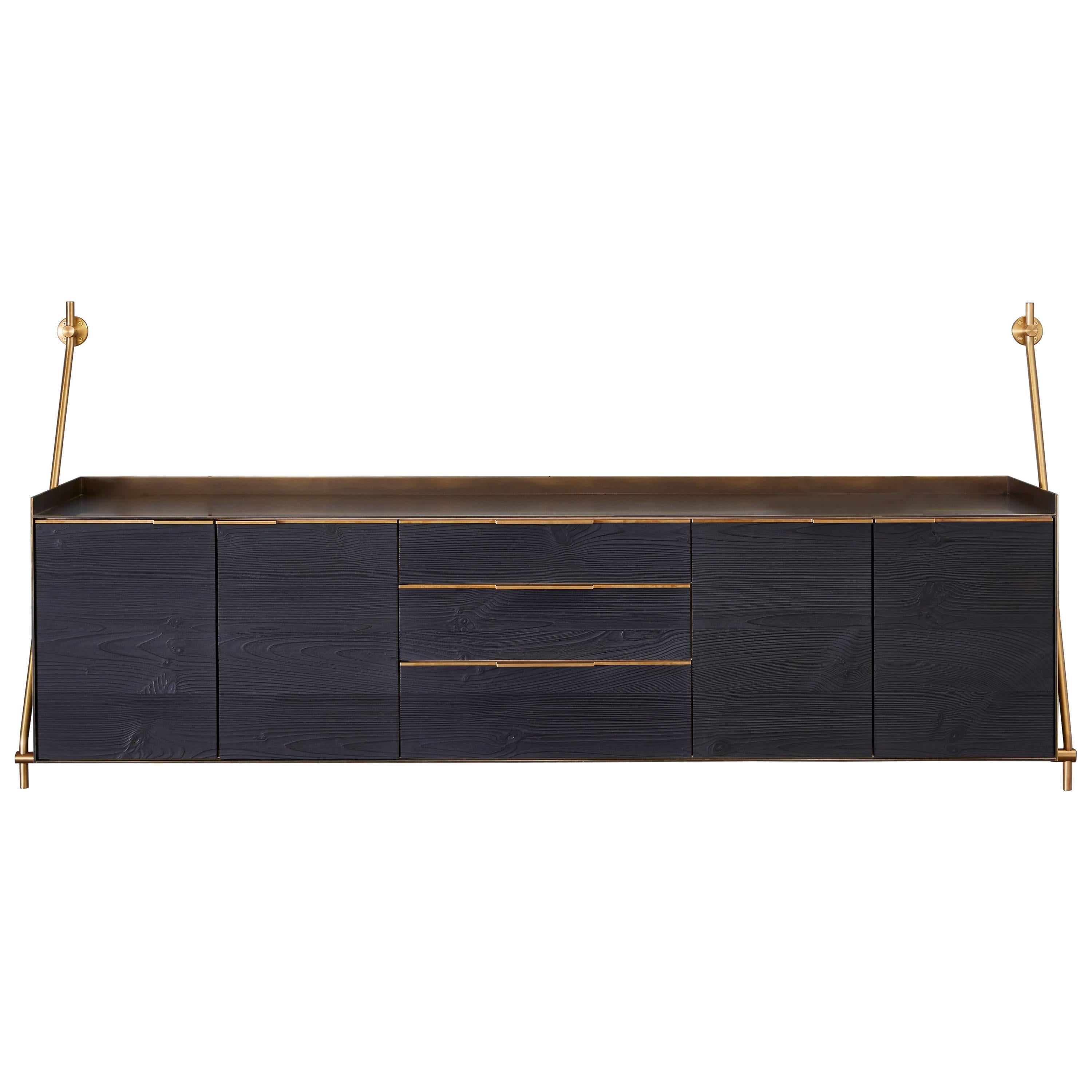 Amuneal’s wall hanging credenza is supported by our traditional collector’s shelving hardware in a warm brass finish. The credenza itself is clad in solid bronze with a deep, mottled, patinated finish with golden highlighted edges. The structure of