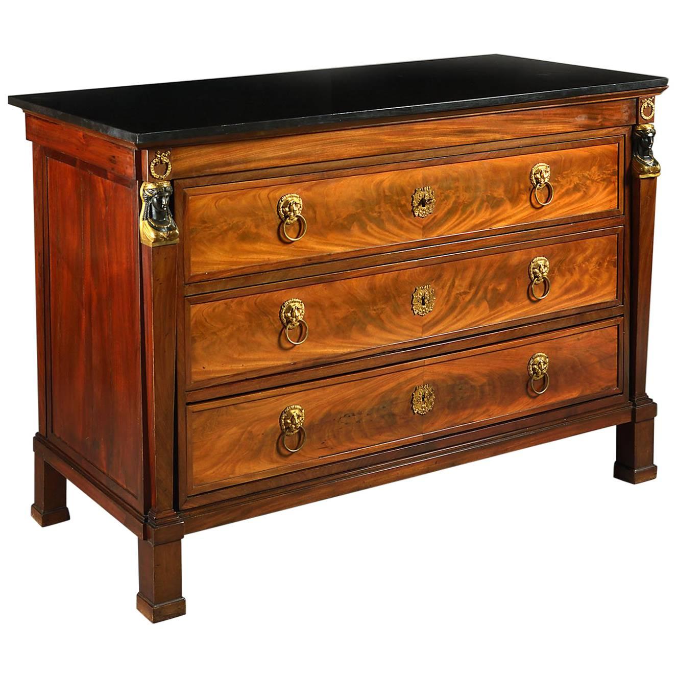 A fine early 19th century mahogany Empire commode with Egyptian caryatids, three graduated drawers, retaining the original fire gilt lion mask handles, with black marble top.