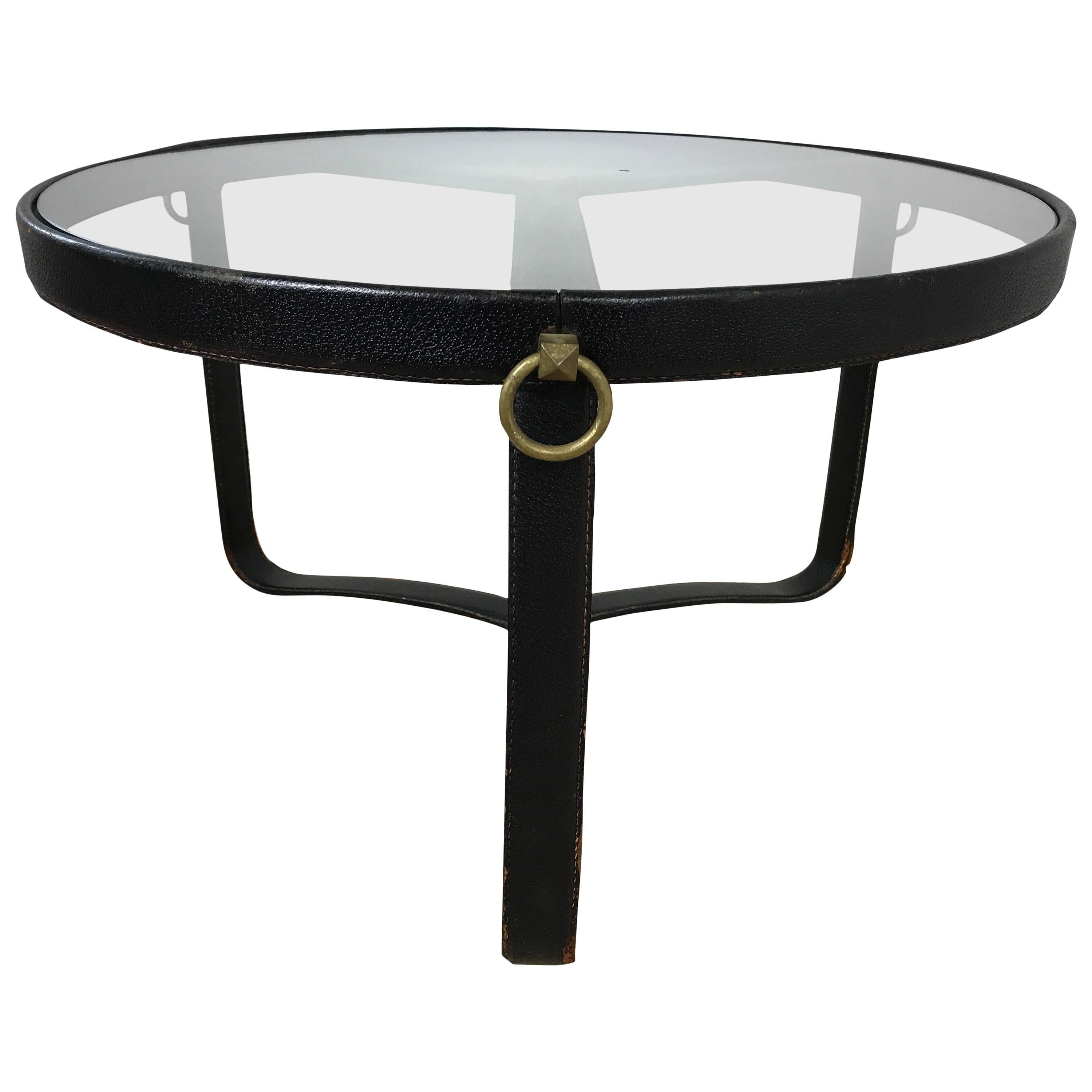 Early and original Jacques Adnet stitched black leather cocktail table with tripod base and brass hardware accents. Original glass top.