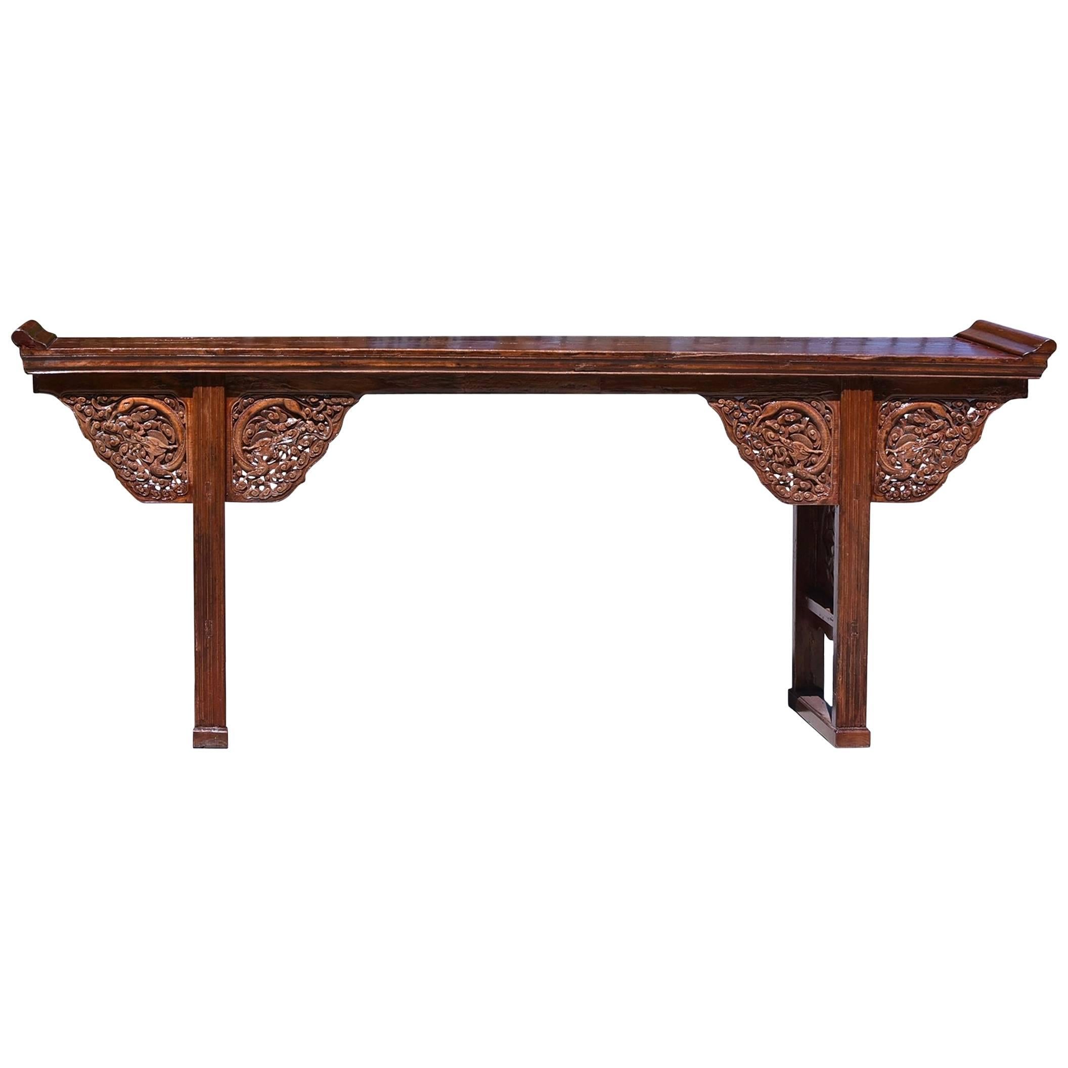 A fantastic Chinese altar with fine, detailed carvings depicting dragons flying in the clouds. The table has a beautiful, reddish top that is made of a single solid board. Its raised flanges pay homage to the Chinese temple architecture. There are