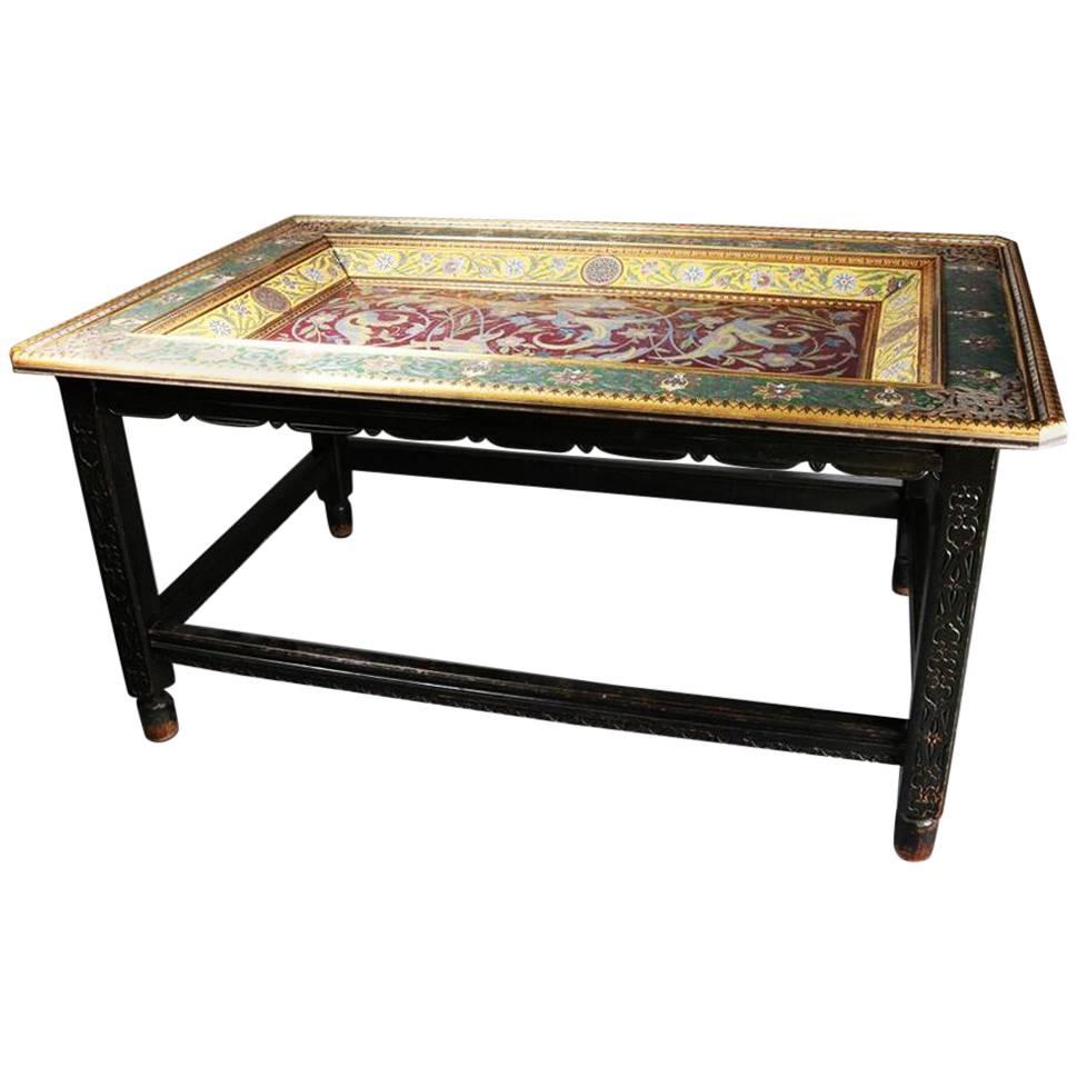 Important and antique Moorish style table features Arabesque recessed and ornately decorated top with Islamic gilt and enameled floral, scroll and foliate rinceaux design on silver atop Chinese carved hardwood base and having a protective glass top,