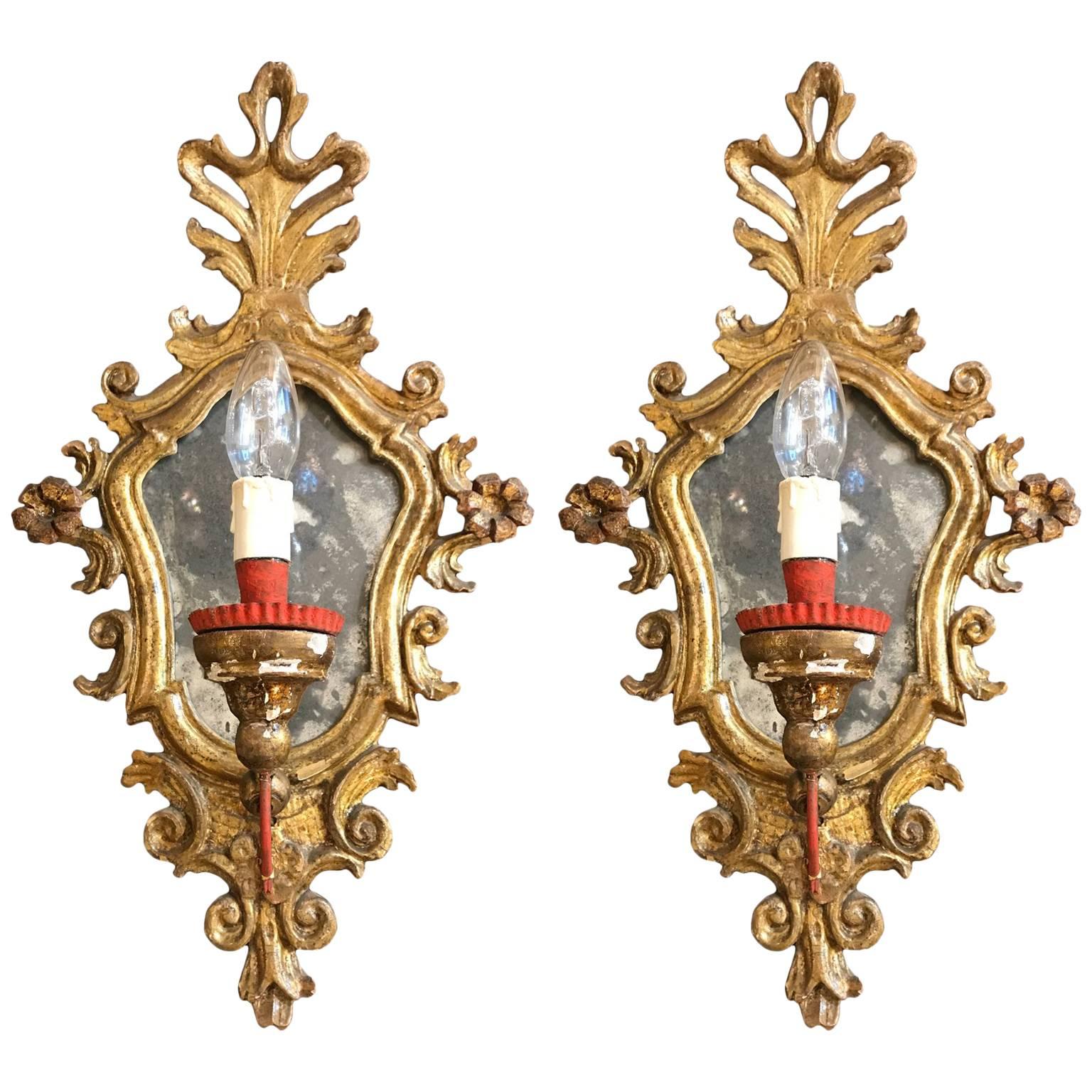 A pair of Italian Louis XV one light wall sconces with original mercury mirror plates within mecca gilded frames, carved with vegetal elements and scrolling  motifs.
In the lower part, one curved wrought iron sconce arm for candle, probably replaced