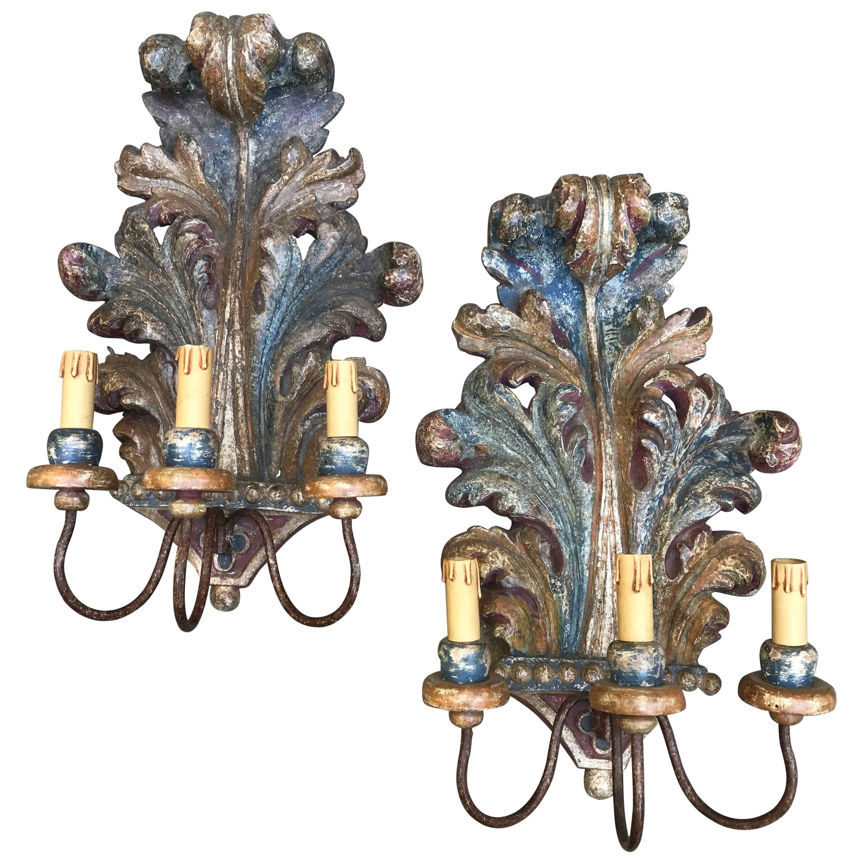 A pair of decorative Italian acanthus leaf carved three-armed wall lights, polychrome painted with shaded blue, pink and ocher, really very delicate colors and silvered traces in the lower pearling center.
Three-light wall sconces with curved iron