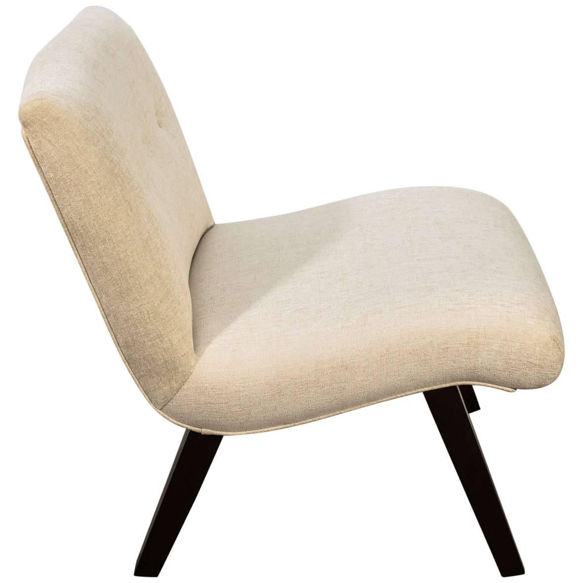 Mid-Century Modern slipper chair with scoop design. The lounge chair has splayed wood legs in a dark walnut finish with visible wood grain. Upholstered in woven crème colored chenille. Features button accents and self-welt details.