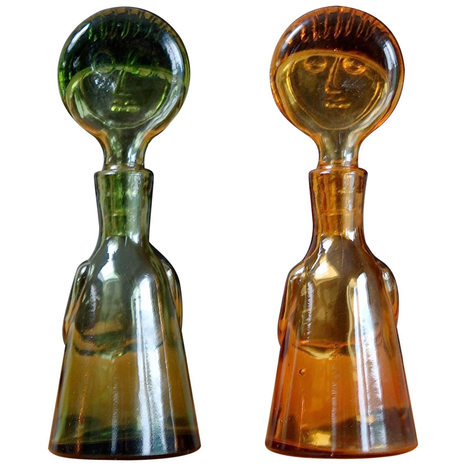 Two miniature bottles colloquially referred to as people or face decanters because of their figurative design. The stopper is in the shape of a head or face and the designer created the illusion of a body by adding arms and hands that clasp