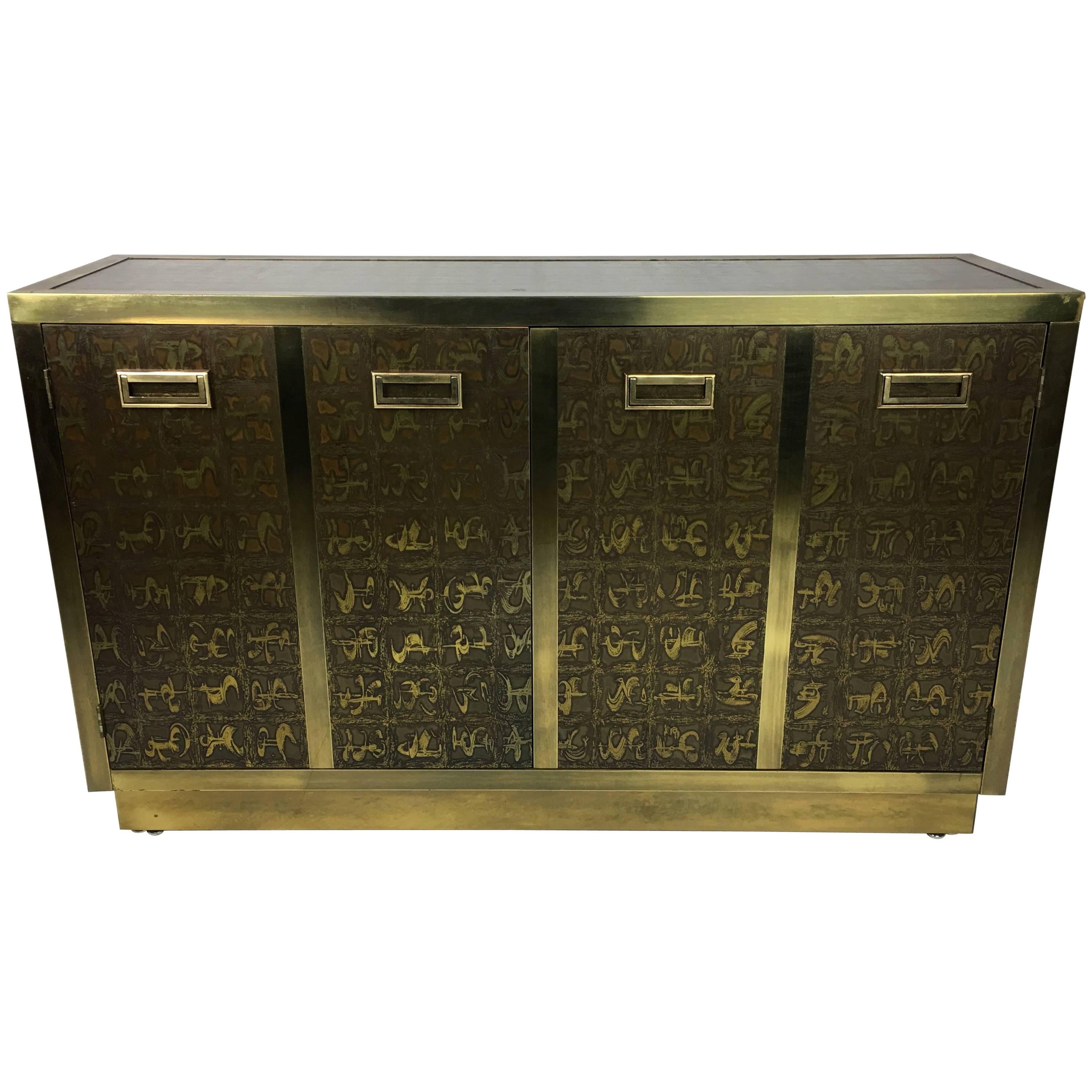 Rare brass clad two-door cabinet decorated with etched abstract figures by Bernard Rohne for Mastercraft. The etched design is featured on three sides and the top of the cabinet. This versatile statement piece would make an excellent Buffet,
