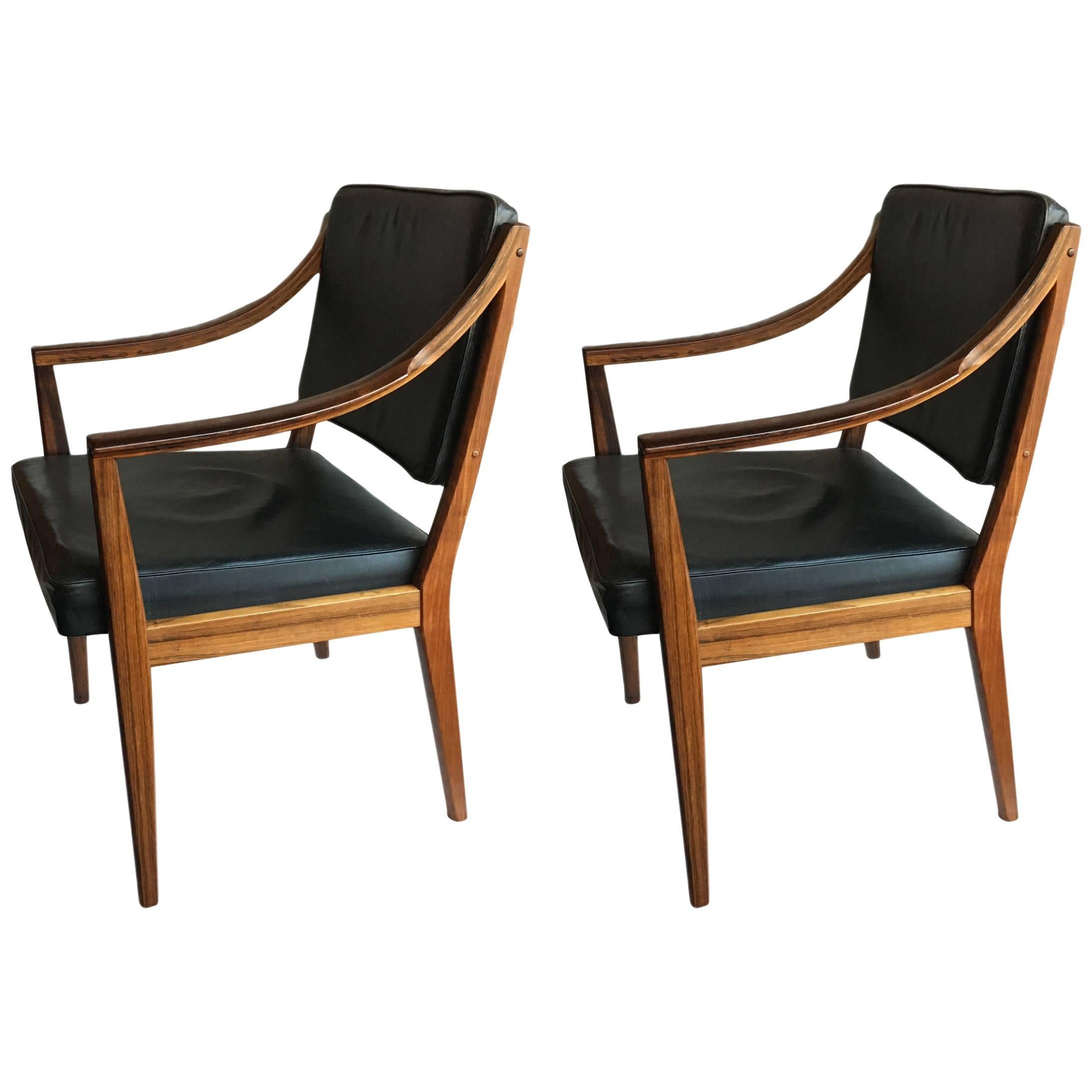 A matching pair of elegant and very unusual Scandinavian Midcentury armchairs. Norwegian in design with beautiful sweeping Santos rosewood arms and original black leather upholstery. The craftsmanship in the build of these chairs is exceptional. We