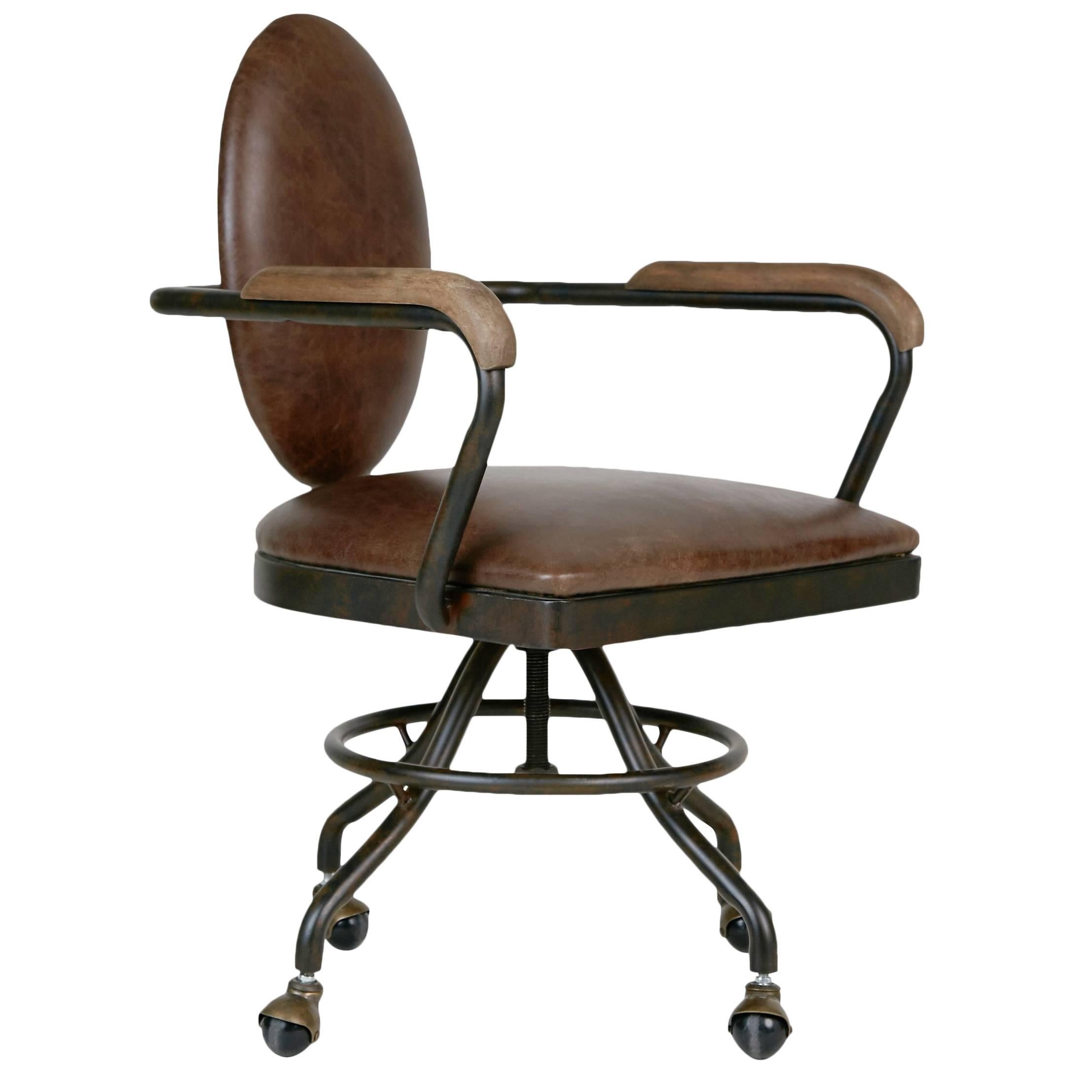 Industrial style desk chair, circa 1930. This sleekly designed office chair features an unusual oval shaped back with contrast nailheads on the reverse. The frame has an antiqued metal finish with smooth wooden armrests and is positioned on casters