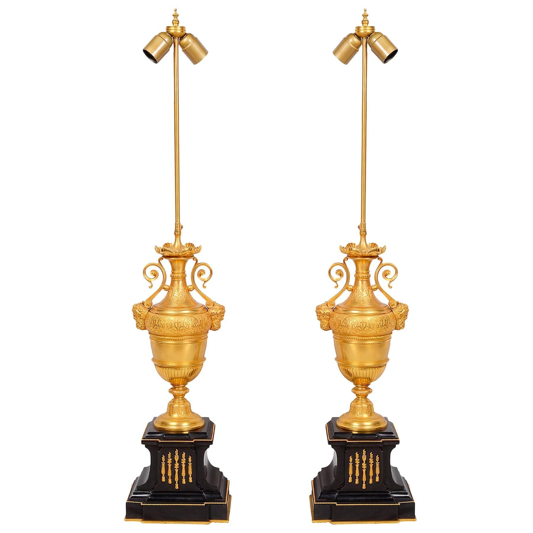 A pair of classical gilded ormolu and marble urn lamps, each with scrolling handles and bearded mask mounts.