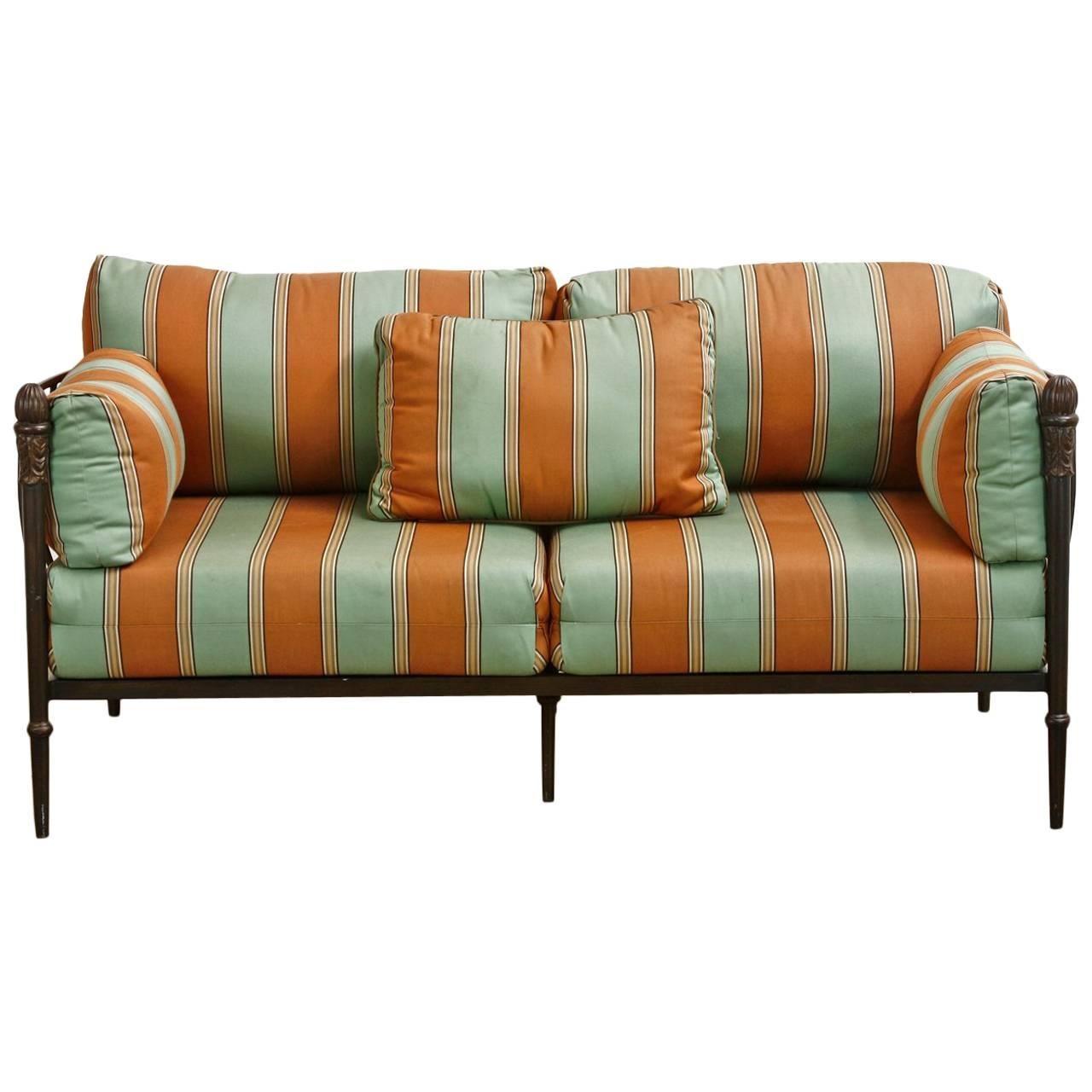 Fabulous Michael Taylor design iron settee or loveseat from his famous Montecito Collection. Features a patinated bronze finish with whimsical striped upholstery. This rare settee has an iron frame that cradles the deep cushions with bowed sides and