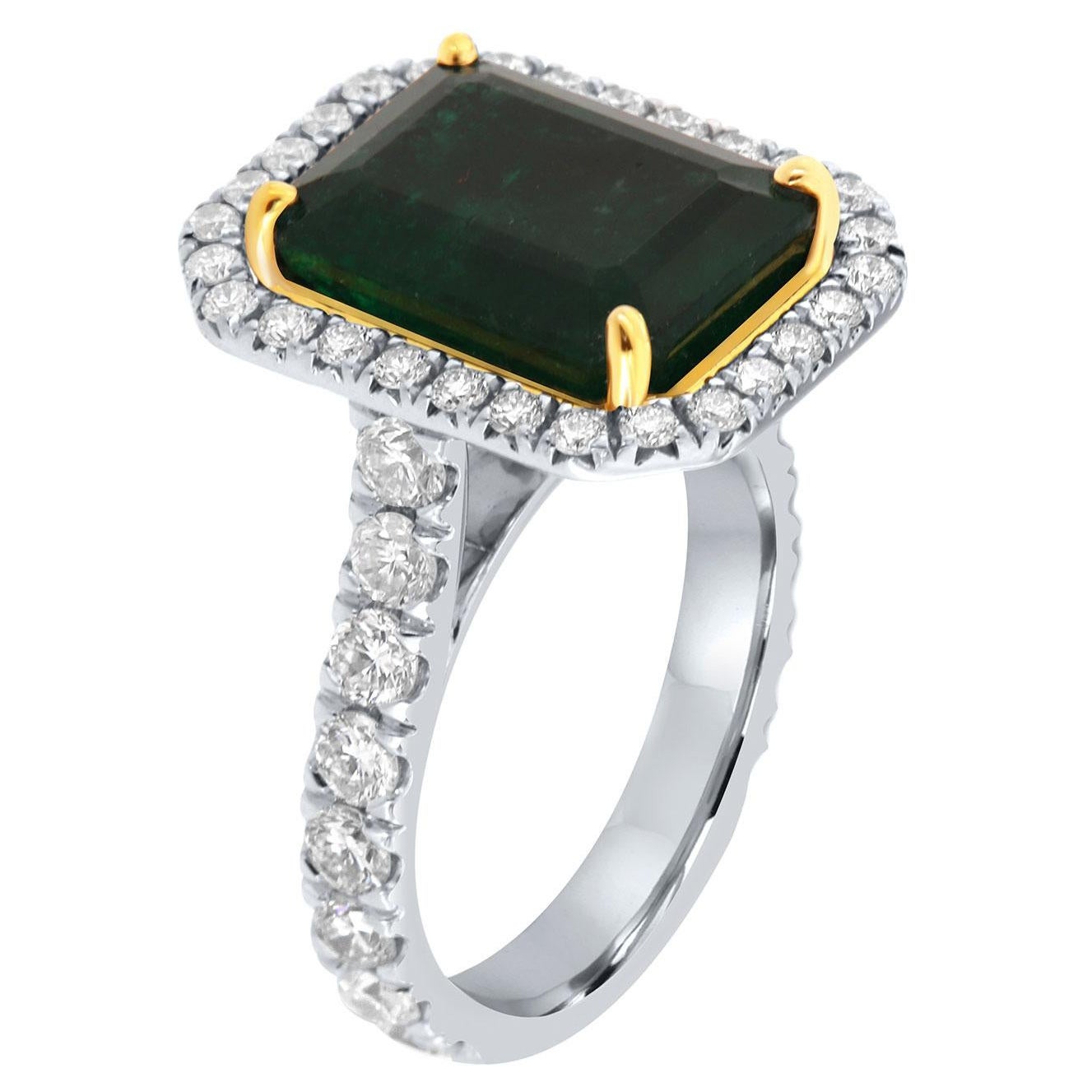 This 18k white and yellow gold ring features a 6.83 Carat Emerald cut Natural Green emerald from Zambia. It is encircled by a halo of brilliant round diamonds on a 3.4 mm wide band. The diamonds are Micro-Prong set on 75% of the band.  The diamond's