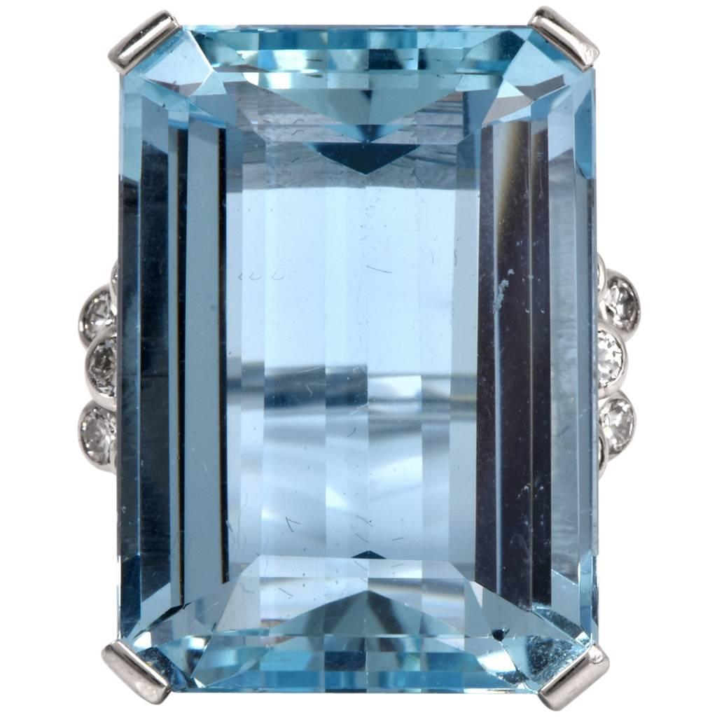 This fine vintage aquamarine ring is hand crafted in solid alluring platinum. It centered with a gorgeous emerald aquamarine gem measuring approx. 23.5 mm x 16.8mm x 10.7mm approx: 28.94 cttw that is complemented by a cluster of 14 genuine round cut