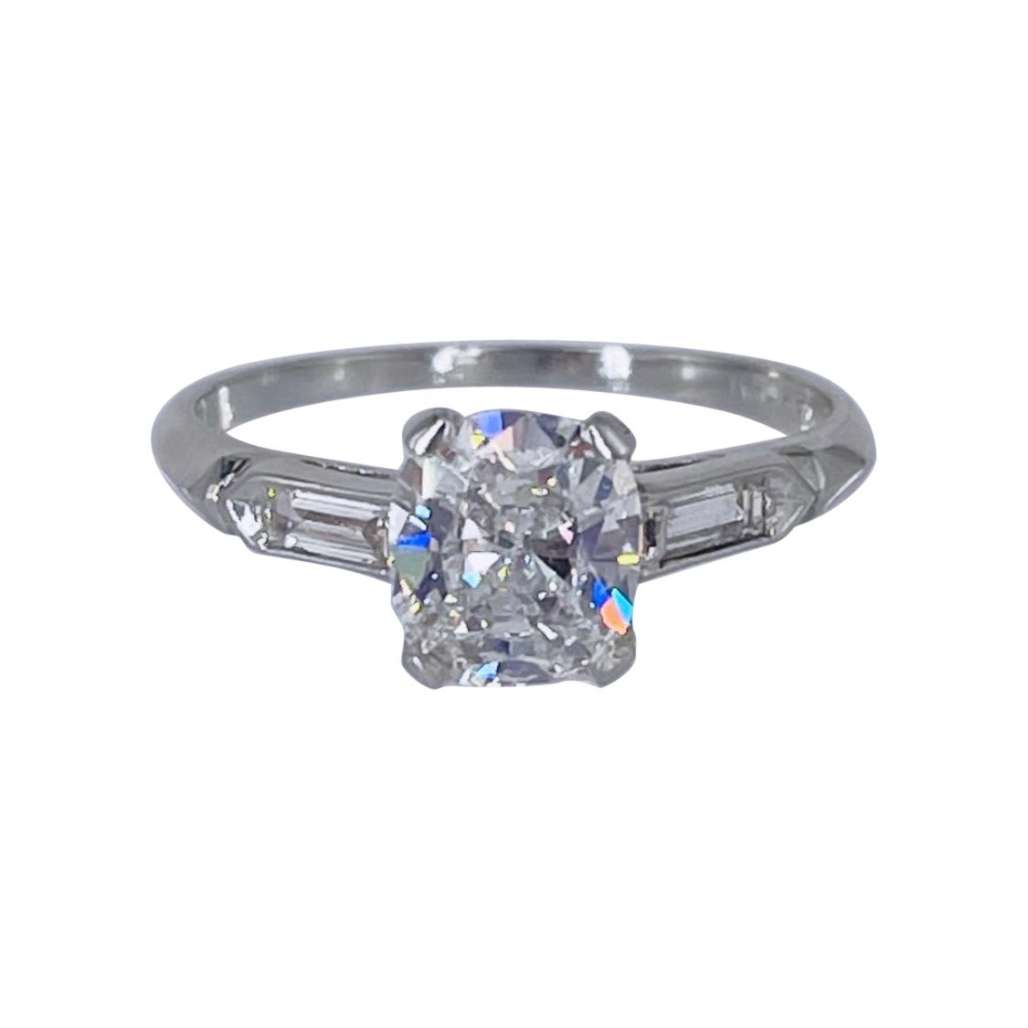 This sparkling engagement ring by J. Birnbach is a charming piece inspired by the Art Deco period. The ring features a 0.92 carat cushion brilliant diamond certified by GIA to be H color and SI1 clarity. The center diamond is accented by two