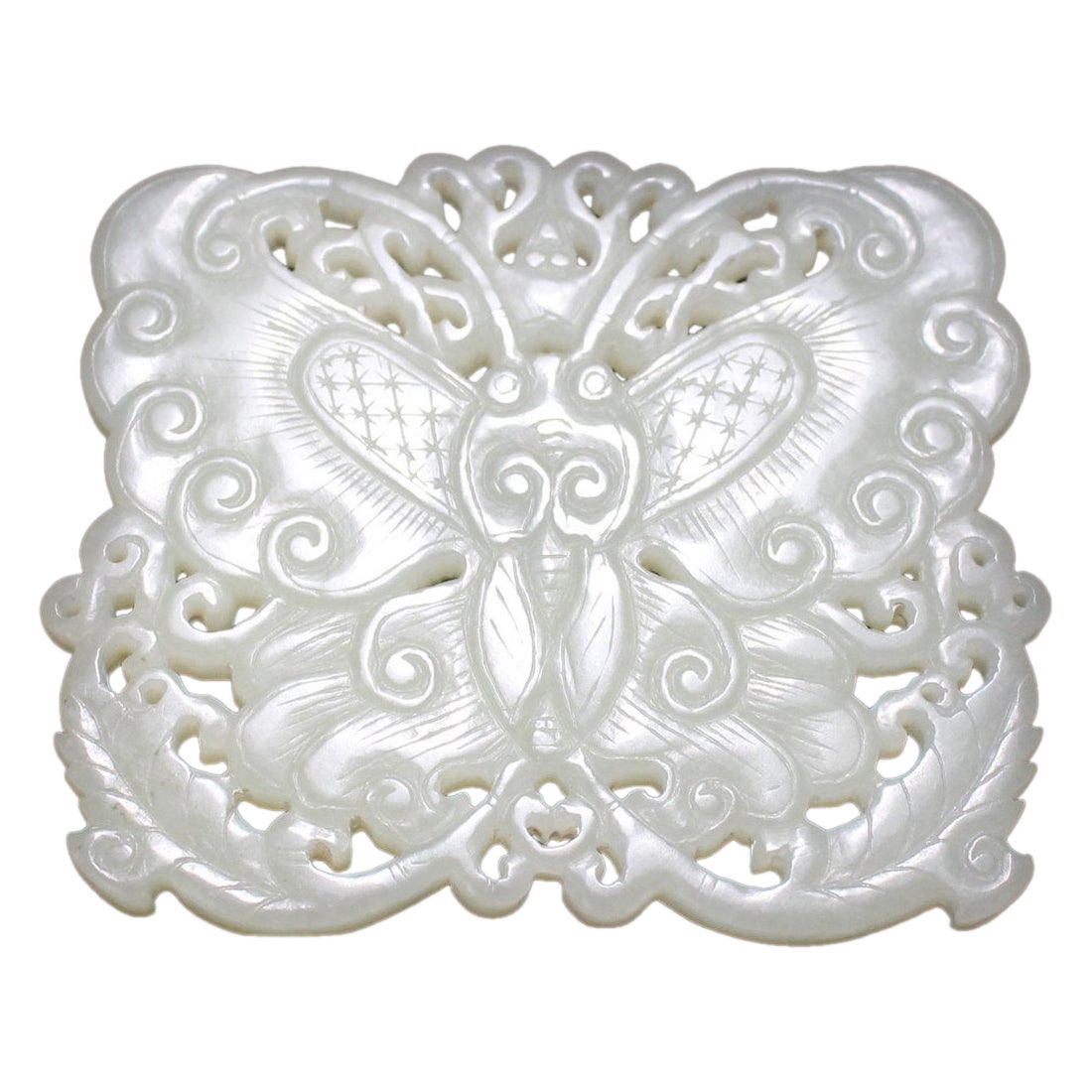 Carved from pale celadon jade, this two-sided Ming Dynasty piece features a butterfly with curling, cloud-like wings and a grid-and-star pattern. Fine lines radiate out from the center, creating an intricate design. Two leaves adorn the bottom,