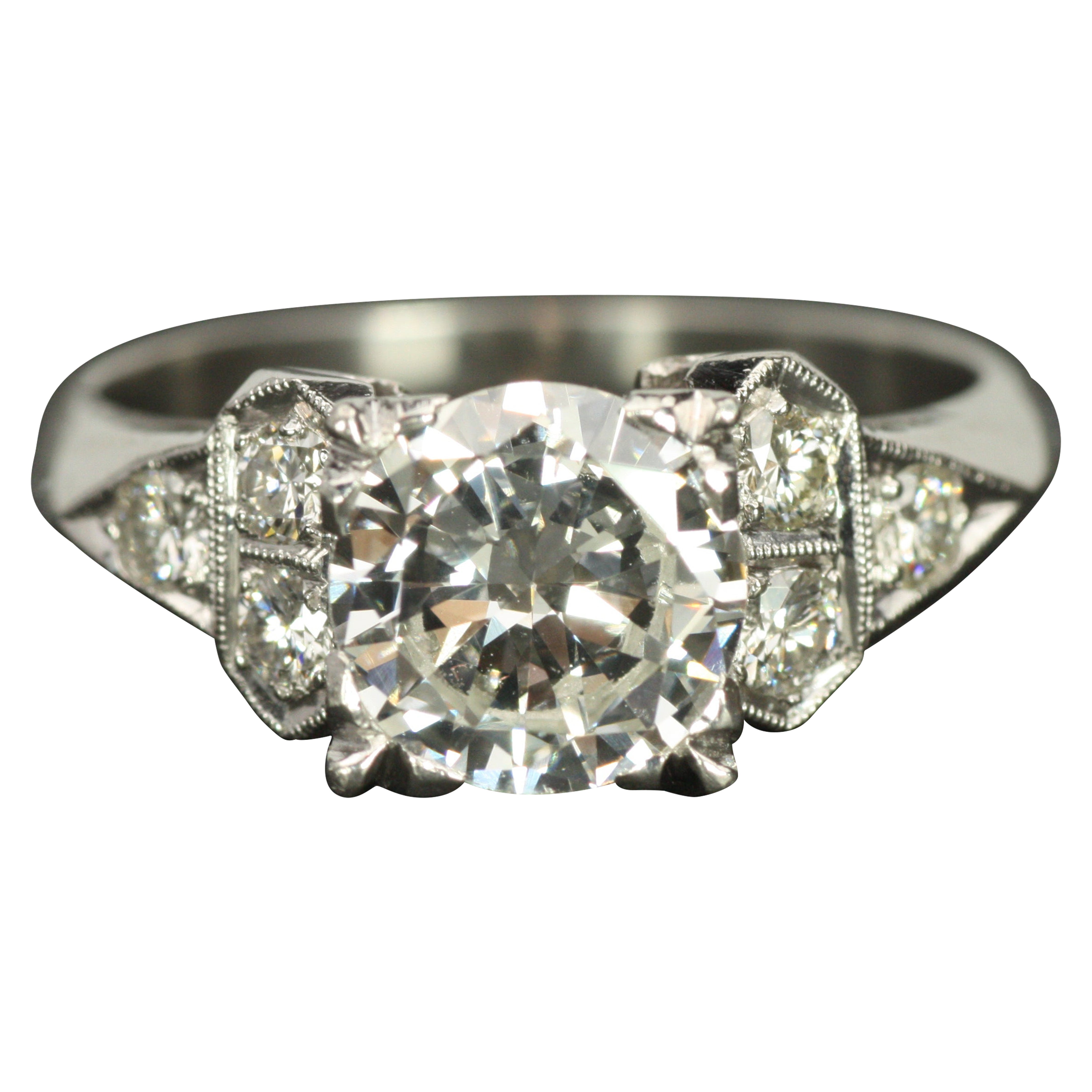 Though crafted in the 1950s, this engagement ring reflects strong Art Deco influences, with geometric designs accentuated by exquisite milgrain detailing. Made in platinum, it features a 1.00ct round center diamond, framed by six surrounding round
