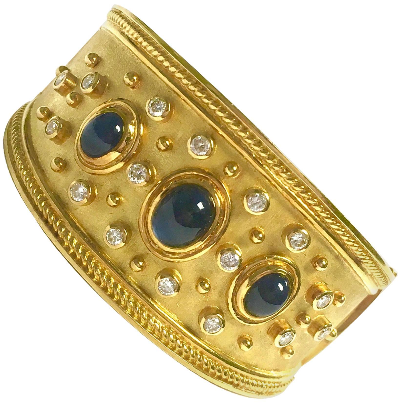 Gorgeous 19K yellow gold hinged bangle bracelet featuring three bezel set oval cabochon cut blue sapphires, approximate total weight 10ct., surrounded by sixteen bezel set round brilliant cut diamonds, approximate total weight: 1.50ct. Color: G-H,
