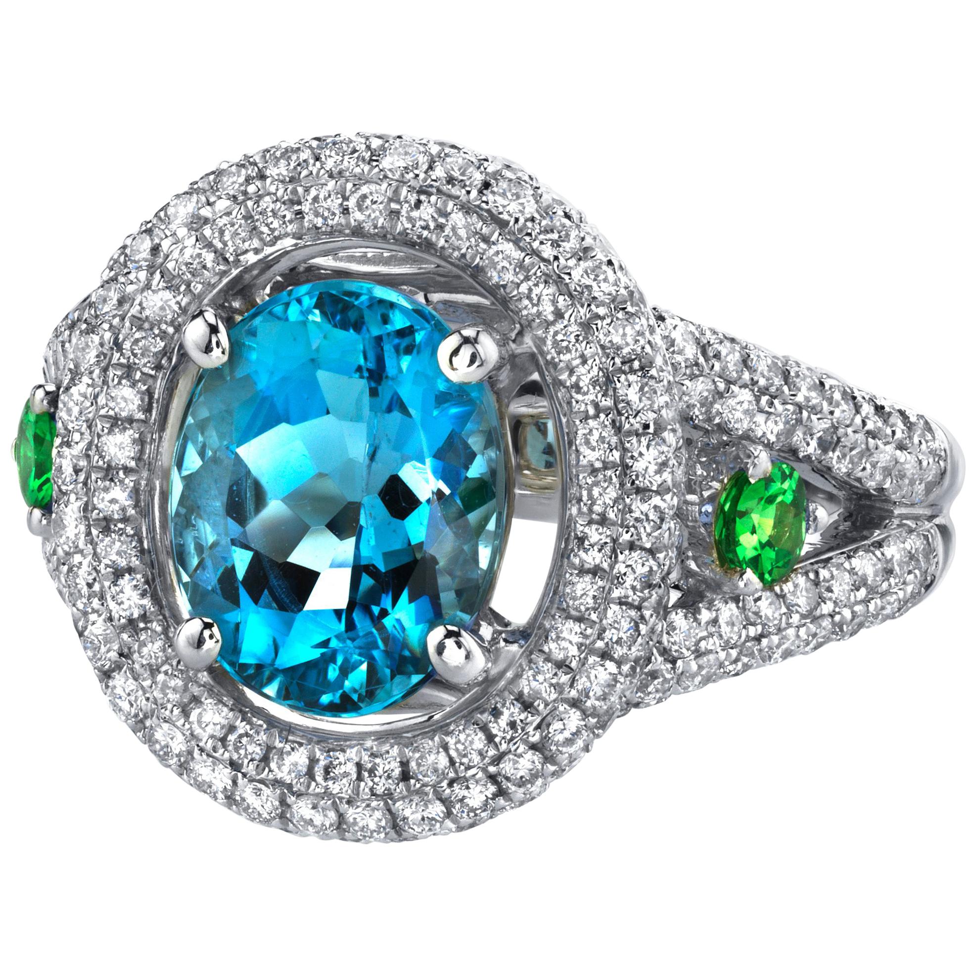 This elegant cocktail ring features a gem-quality aquamarine oval surrounded by a double diamond halo and accented with bright tsavorite garnets set in 18k white gold. The center aquamarine is an unusually fine gem with extraordinary deep blue color