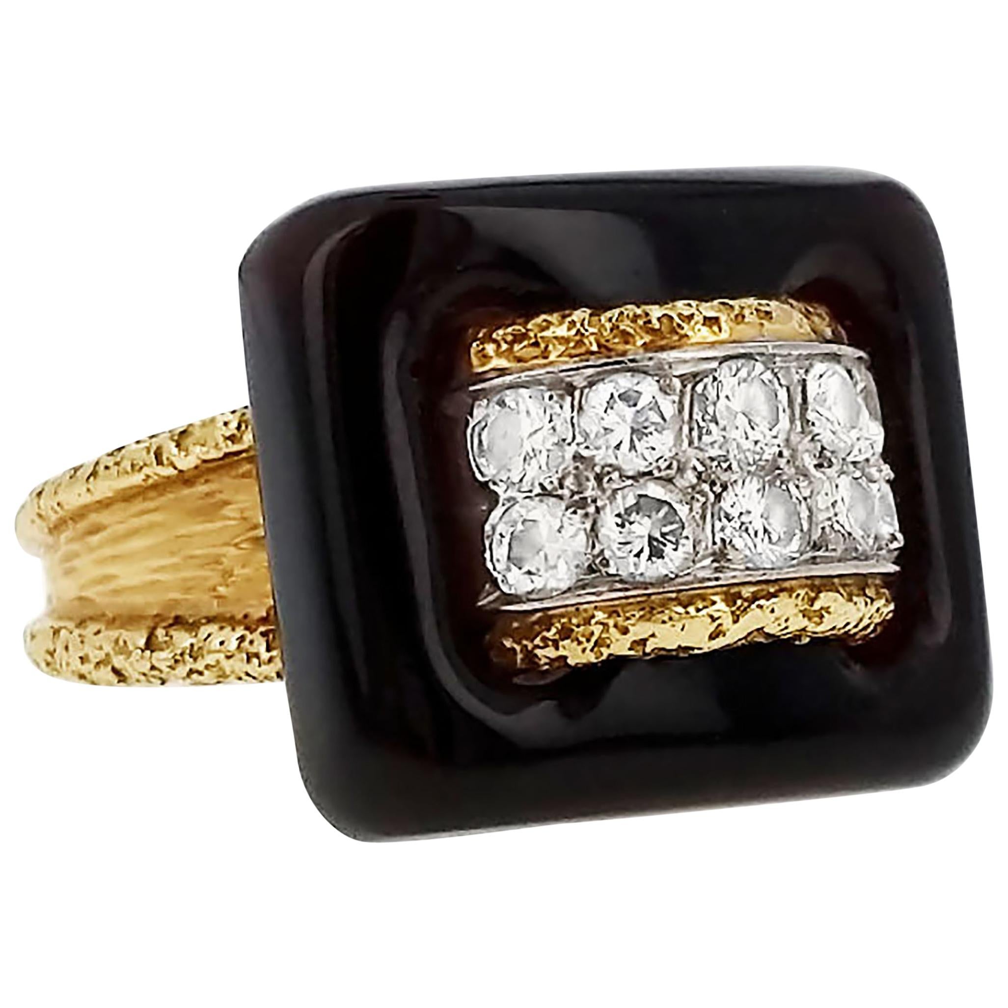A ring centering upon a smooth onyx buckle-like plaque, woven through with a round-cut diamond pave 