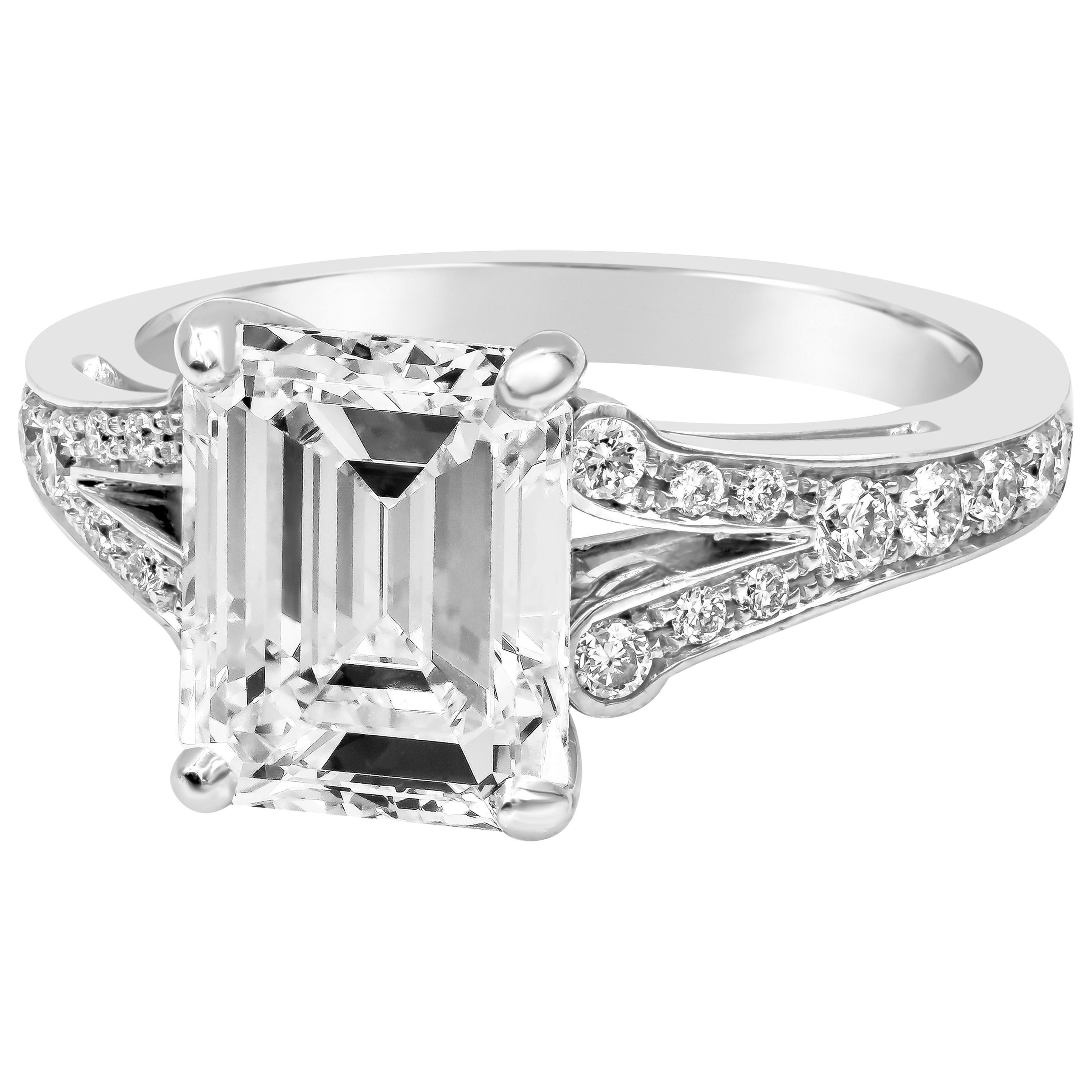Elle présente un diamant de 3,01 carats de taille émeraude certifié par la GIA de couleur E et de pureté VS2, serti dans une monture en platine à deux branches accentuée par des diamants ronds de taille brillant de chaque côté. Les diamants