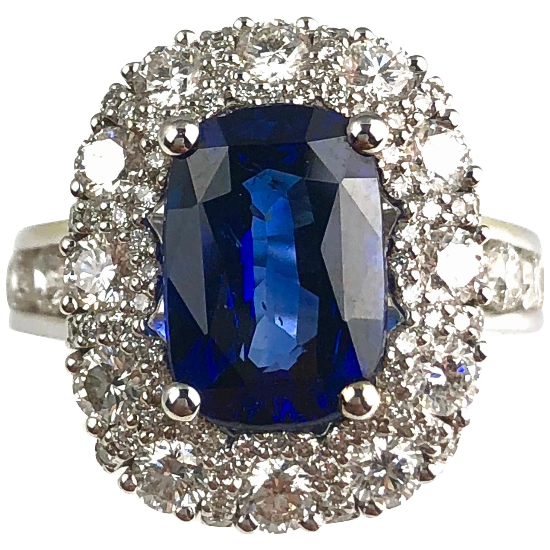 (DiamondTown) A 4.04 carat cushion cut fine Sapphire center, surrounded by a decorated halo of round white diamonds, creates an elegant look for this classic ring Smaller round diamonds fill in the spaces between the 12 main diamonds of the halo.