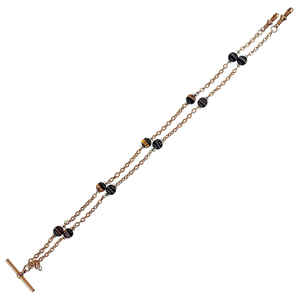 A dapper accessory for the well-dressed gent, this 9 karat gold Albert chain is decorated with carved orbs of banded agate bordered by rock crystal rondelles. The toggle at the center was deigned to secure the chain to a button hole and the two